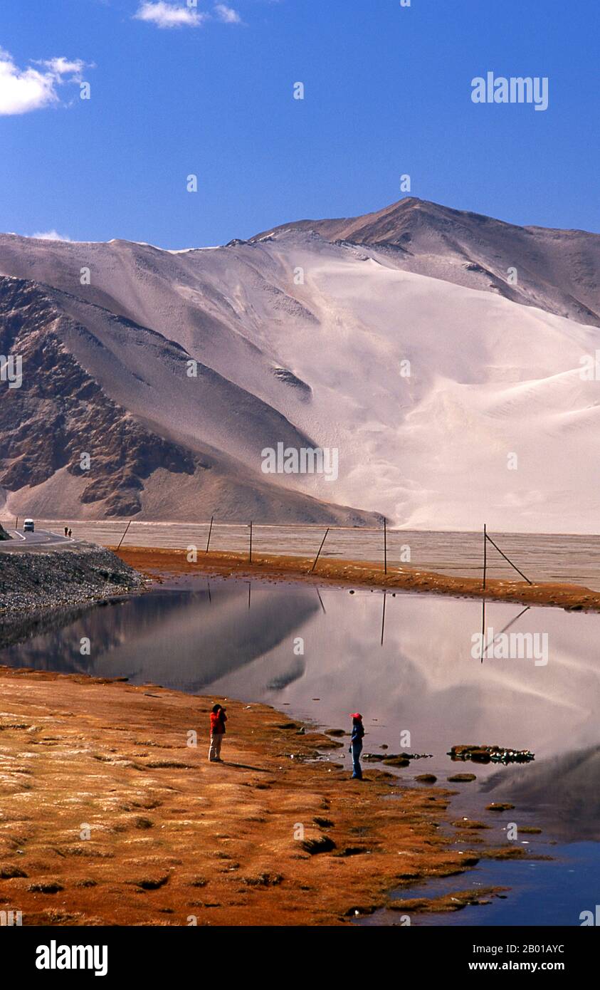 China: Touristen in der Nähe des Kangxiwa Flusses hoch oben im Pamir Gebirge, Karakorum Highway, Xinjiang. Die Pamir-Berge sind eine Gebirgskette in Zentralasien, die durch die Kreuzung oder den Knoten der Himalaya-, Tian Shan-, Karakoram-, Kunlun- und Hindu-Kush-Gebirge gebildet wird. Sie gehören zu den höchsten Bergen der Welt und sind seit viktorianischer Zeit als „Dach der Welt“ bekannt, eine wahrscheinliche Übersetzung aus dem Persischen. Der Zhongba Gonglu oder Karakoram Highway ist ein Ingenieurswunder, das 1986 eröffnet wurde und die höchste asphaltierte Straße der Welt bleibt. Sie verbindet China und Pakistan. Stockfoto