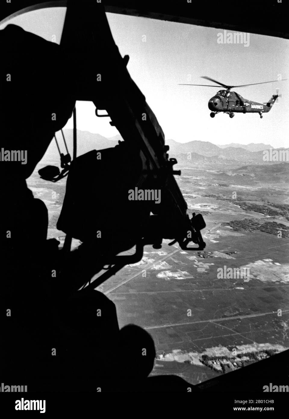 Vietnam: Blick aus der Position des Türschützers aus den USA Marine Corps Sikorsky UH-34D Seepferd-Hubschrauber über Vietnam; im Vordergrund steht das M-60-Maschinengewehr des Schützen, ca. 1965. Der zweite Indochina-Krieg, in Amerika als Vietnamkrieg bekannt, war ein militärischer Konflikt aus der Zeit des Kalten Krieges, der sich in Vietnam, Laos und Kambodscha vom 1. November 1955 bis zum Fall Saigons am 30. April 1975 ereignete. Dieser Krieg folgte dem ersten Indochina-Krieg und wurde zwischen Nordvietnam, unterstützt von seinen kommunistischen Verbündeten, und der Regierung von Südvietnam, unterstützt von den USA und anderen antikommunistischen Nationen, geführt. Stockfoto
