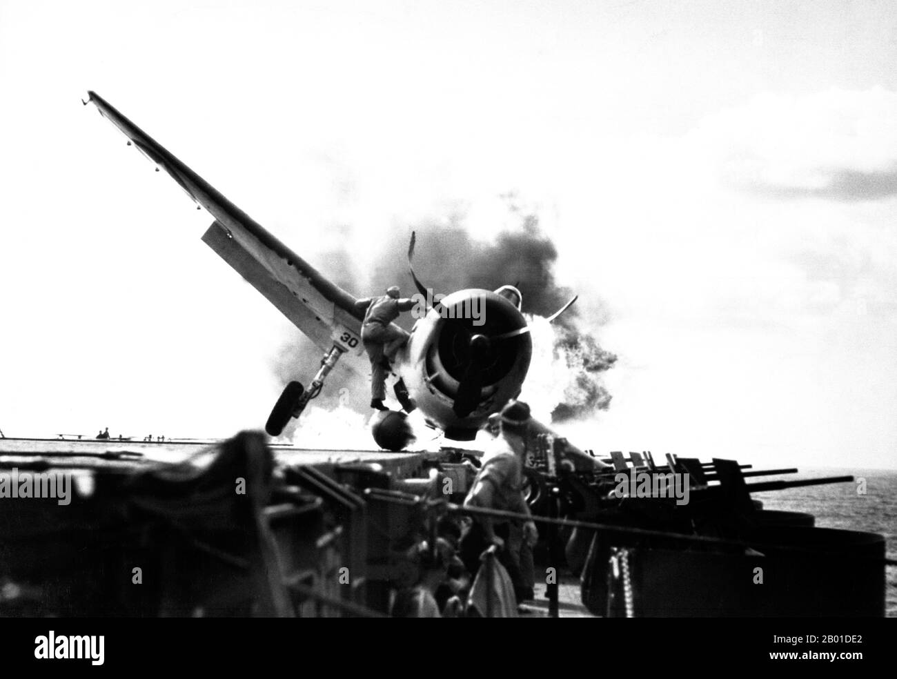 USA/Japan: Ein USAF F6F-3 Crash landete auf dem Deck der USS Enterprise, 10. November 1943. Crash Landung von F6F auf dem Flugdeck der USS Enterprise während des Angriffs auf Makin Island. LT. Walter Chewning, Katapult-Offizier, klammert die Seite des Flugzeugs hoch, um dem Piloten, Fähnrich Byron Johnson, aus dem brennenden Cockpit zu helfen. Stockfoto