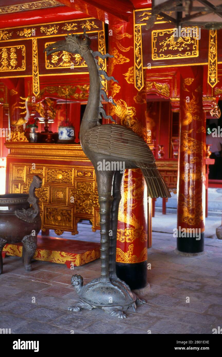 Vietnam: Ein Bronzekranich steht auf einer Schildkröte vor dem Altar des Konfuzius, dem Großen Zeremoniehaus, dem Literaturtempel (Van Mieu), Hanoi. Der Literaturtempel oder Van Mieu ist einer der bedeutendsten kulturellen Schätze Vietnams. Der Tempel wurde 1070 von König Ly Thanh Tong aus der frühen Ly-Dynastie gegründet und war ursprünglich Konfuzius und Chu Cong gewidmet, einem Mitglied der chinesischen Königsfamilie, dem viele der Lehren, die Konfuzius fünfhundert Jahre später entwickelte, zugeschrieben wurden. Stockfoto