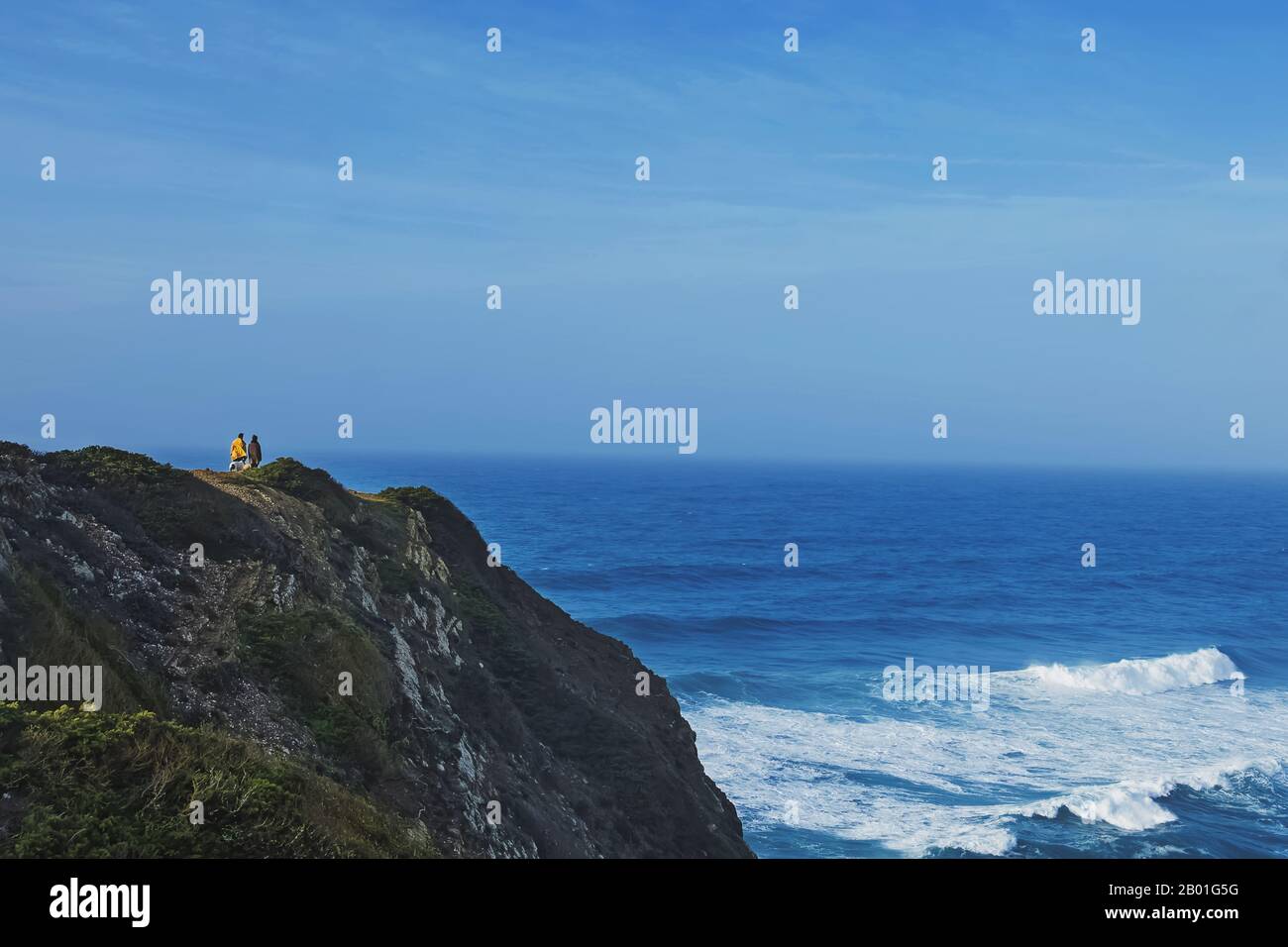 Kleines Sigluestea von Paar und Hund, das auf der Klippe steht und zu Wellen auf dem Ozean schwand Stockfoto