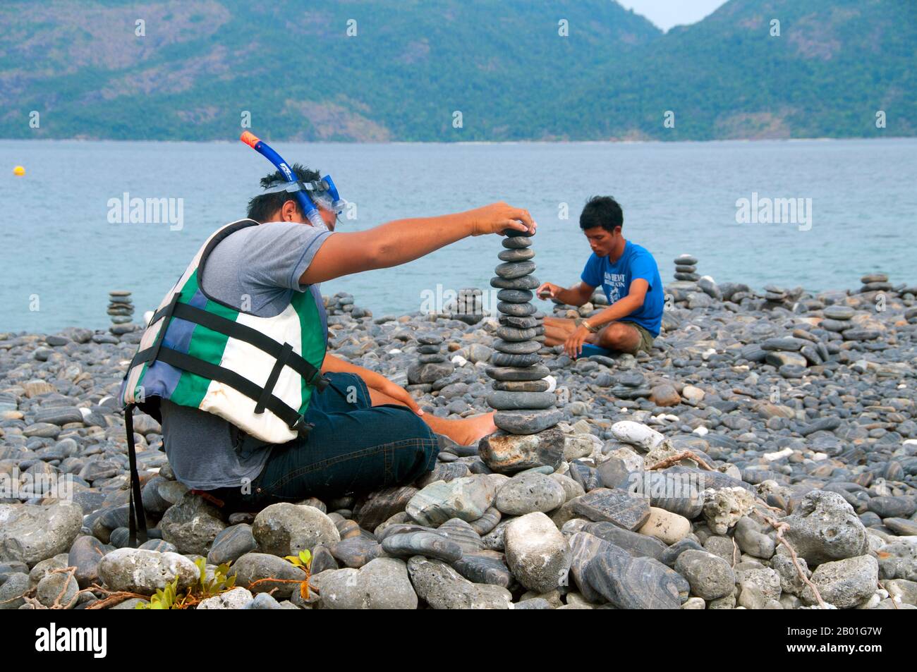 Thailand: Besucher am Kieselstrand, Ko hin Ngam, Ko Tarutao Marine National Park. Ko hin Ngam bedeutet auf Thai „Insel der schönen Steine“, und der kleine Strand ist mit glatten schwarzen Steinen in verschiedenen Formen bedeckt und mit charakteristischen Mustern bedeckt. Der Marine-Nationalpark Ko Tarutao besteht aus 51 Inseln in zwei Hauptgruppen, die über die Andamanensee im südlichsten Thailand verstreut sind. Nur sieben der Inseln haben jede Größe, einschließlich Ko Tarutao im Osten und Ko Adang-Ko Rawi im Westen. Nur 5 Meilen (8km km) südlich liegt die Meeresgrenze mit Malaysias gefeiertem Langkawi-Archipel. Stockfoto