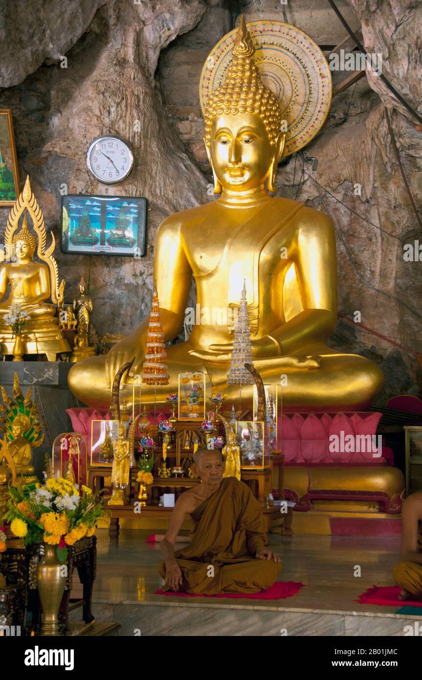 Thailand: Mönch und Buddha, Wat Tham Seua, Krabi-Stadt, Provinz Krabi, Südthailand. Wat Tham Seua, der „Tempel der Tigerhöhle“, ist in eine Höhle in einer Kalksteinklippe gebaut. Umgeben von einzelnen Mönchsresidenzen ist dies einer der bekanntesten Waldtempel im Süden Thailands. Die Haupt-Viharn- oder Montagehalle erstreckt sich in eine lange, flache Kalksteinhöhle, die verschiedene düstere Erinnerungen an die Sterblichkeit als Gegengewicht zu weltlichen Wünschen zeigt. Hinter der Höhle führt eine Marmortreppe hinauf zur „Tigerhöhle“ selbst. Stockfoto
