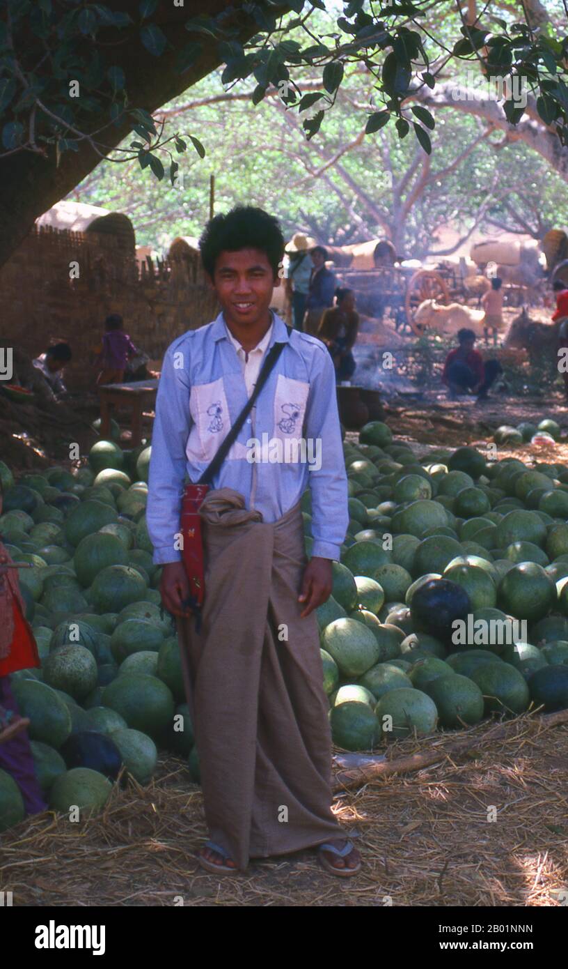 Birma/Myanmar: Wassermelonenverkäufer in der Nähe von Pindaya, Bundesstaat Shan. Ein Longyi ist ein Tuch, das in Burma weit getragen wird. Sie beträgt ca. 2 m (6½ ft.) Lang und 80 cm (2½ ft.) Breit. Das Tuch wird oft in eine zylindrische Form genäht. Es wird um die Taille getragen und läuft bis zu den Füßen. Es wird durch Umklappen des Gewebes ohne Knoten gehalten. Manchmal wird er auch bis zum Knie gefaltet, um Komfort zu bieten. Ähnliche Kleidungsstücke finden sich in Indien, Bangladesch, Sri Lanka und dem Malaiischen Archipel. Auf dem indischen Subkontinent (Bangladesch, Westbengalen, Südindien und Sri Lanka) wird er als Lungi oder longi bezeichnet. Stockfoto