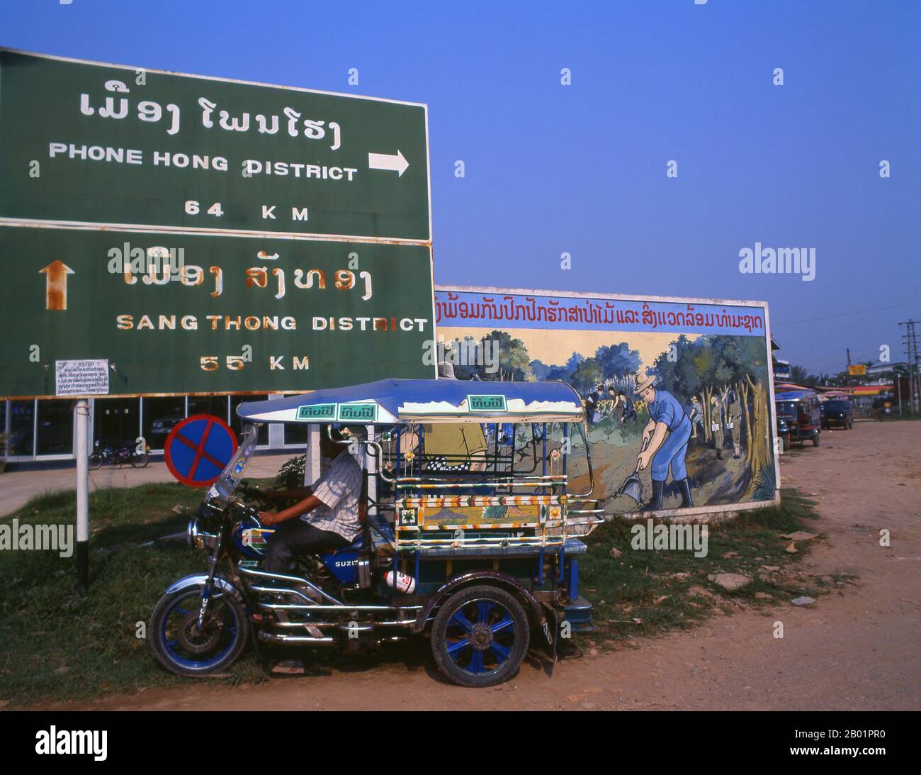 Laos: Ein laotischer Jumbo (Nahverkehr) vor einem politischen Poster im Stil der Revolutionären Sozialisten auf den Straßen von Vientiane. Der sozialistische Realismus ist ein Stil realistischer Kunst, der in der Sowjetunion entwickelt wurde und in anderen kommunistischen Ländern zu einem dominierenden Stil wurde. Der sozialistische Realismus ist ein teleologisch orientierter Stil, dessen Ziel die Förderung der Ziele des Sozialismus und des Kommunismus ist. Obwohl sie damit verbunden ist, darf sie nicht mit dem sozialen Realismus verwechselt werden, einer Art von Kunst, die Themen sozialer Belange realistisch darstellt. Stockfoto