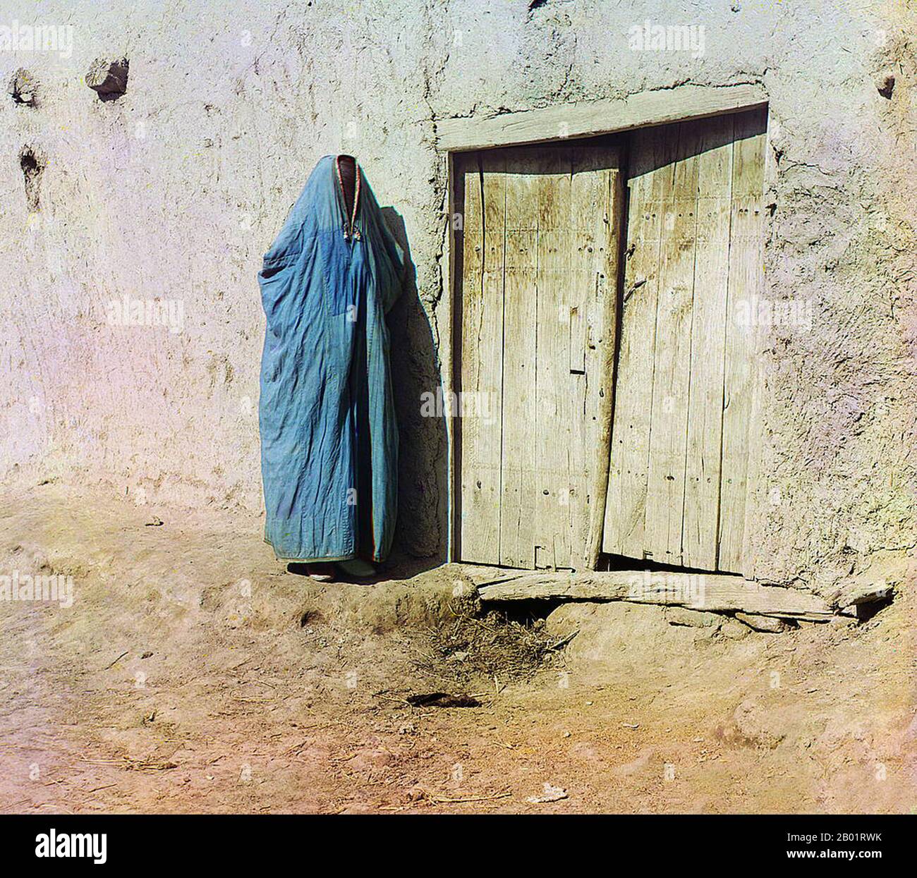 Usbekistan: "SART Woman. Samarkand. Eine Frau in Purdah, die neben einer Holztür steht. Foto von Sergej Michailowitsch Prokudin-Gorskii (31. August 1863 - 27. September 1944), ca. 1905-1915. Eine Paranja oder Paranji, auf Arabisch als „Burka“ bekannt, ist ein traditionelles zentralasiatisches Gewand für Frauen, das sie von Kopf bis Fuß umhüllt. In den 1800er Jahren mussten Frauen der Tadschiken und usbekischen Muslime Paranja tragen, wenn sie außerhalb ihres Hauses waren. Während der Sowjetunion wurden sie verboten, obwohl einige Usbeken sich gewaltsam gegen die Paranja wandten. Heutzutage tragen die meisten zentralasiatischen Frauen keine Paranja. Stockfoto