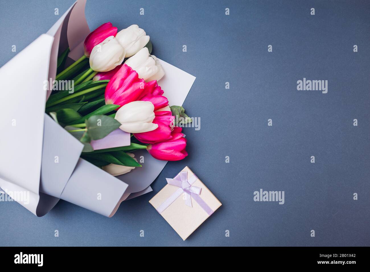 Frühlingsblumen mit Geschenkbox. Hintergrund des Frauentages. Blumenstrauß aus weißen und pingenden Tulpen. Geschenk für den Muttertag Stockfoto