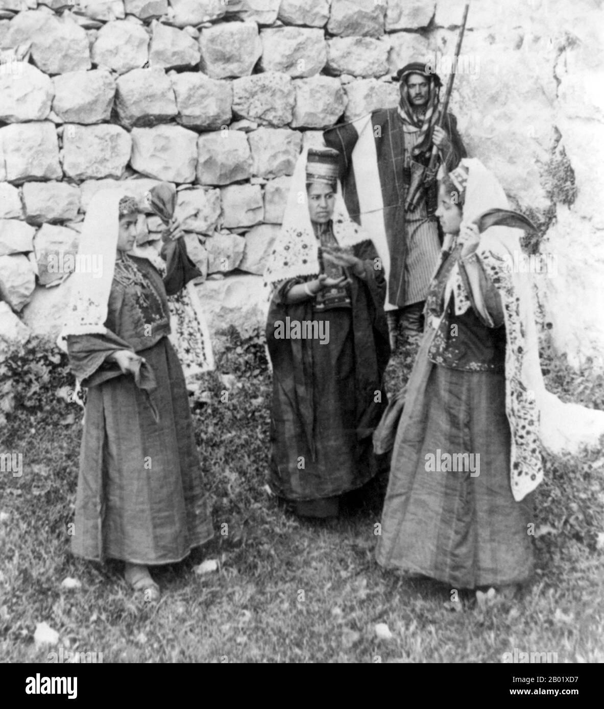 Palästina: Junge palästinensische Mädchen tanzen, während eine ältere Frau die Zeit klatscht und ein Mann mit einem Gewehr bewaffnet über den Tatort wacht. Bethlehem, ca. 1900. Palästina ist ein Name für die geografische Region zwischen dem Mittelmeer und dem Jordan. Die Region ist auch als das Land Israel, das Heilige Land und die Südlevante bekannt. 1832 wurde Palästina von Mohammed Alis Ägypten erobert, aber 1840 intervenierte Großbritannien und gab die Kontrolle über die Levante an die Osmanen zurück, als Gegenleistung für weitere Kapitulationen. Am Ende des 19. Jahrhunderts begann die zionistische Einwanderung. Stockfoto