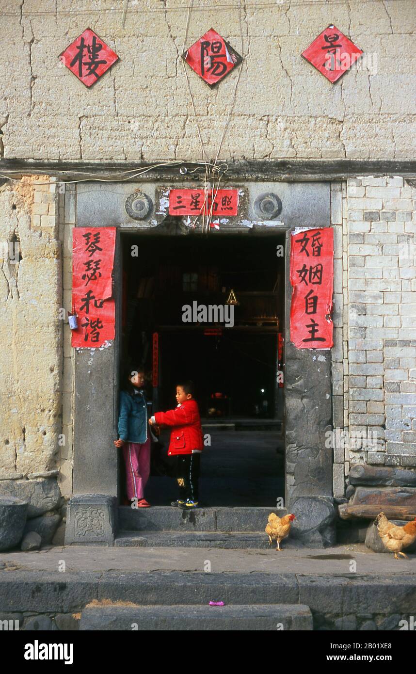 China: Kinder am Eingang zu ihrem Platz Hakka Tower (tulou) in der Nähe von Hukeng, County Yongding, Provinz Fujian. Die Hakka (Kejia auf Mandarin; wörtlich „Gastmenschen“) sind Han-Chinesen, die die Hakka-Sprache sprechen. Die unverwechselbaren Erdhäuser oder tulou befinden sich in den Grenzbezirken, in denen sich die Provinzen Guangdong, Jiangxi und Fujian treffen. tulou sind gegen plündernde Banditen befestigt und bestehen im Allgemeinen aus verdichteter Erde, Bambus, Holz und Stein. Sie enthalten viele Räume auf mehreren Etagen, so dass mehrere Familien zusammen leben können. Stockfoto