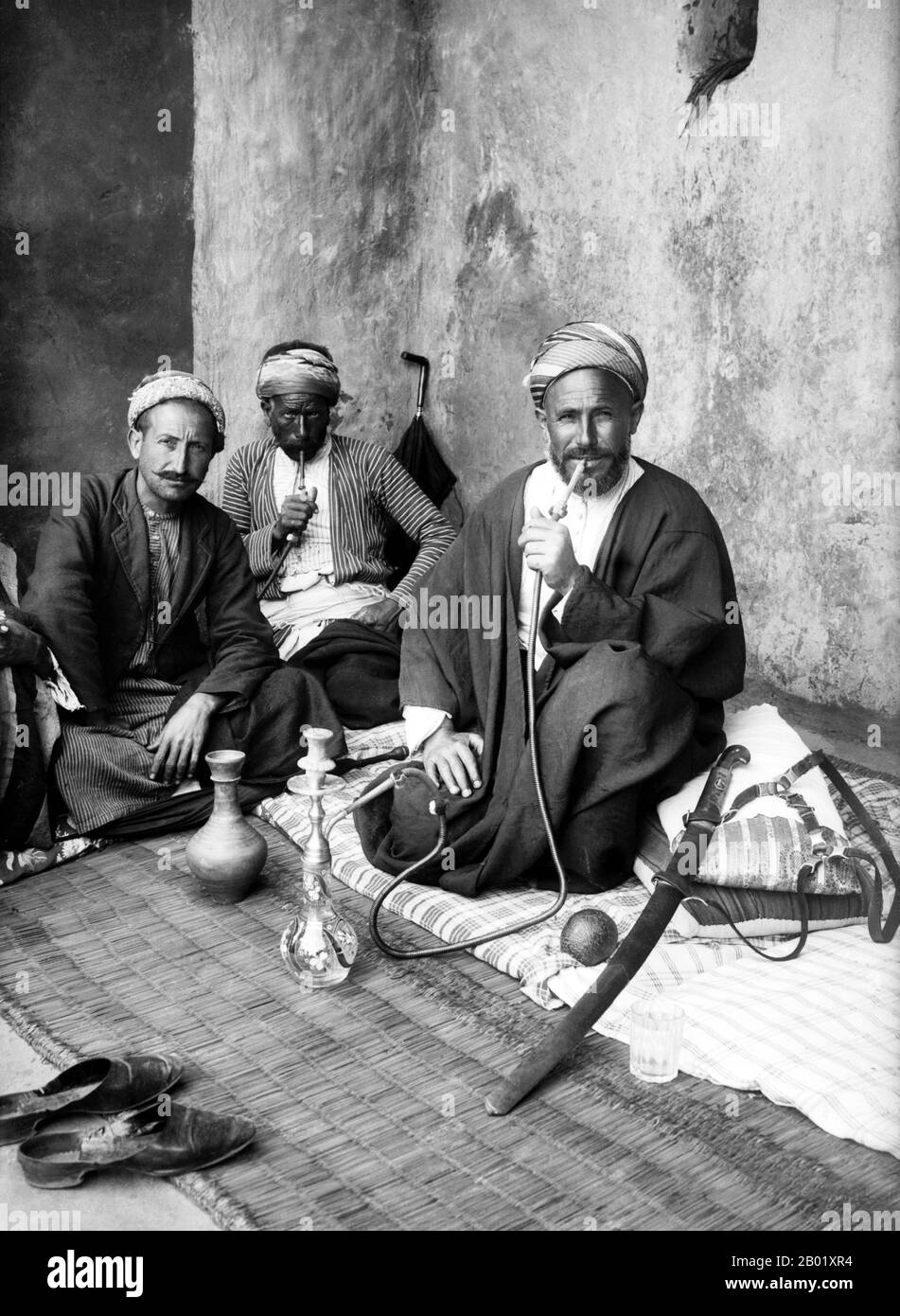 Palästina: Palästinensische Männer, die sich in einem Jerusalem-Kaffeehaus entspannen, während sie Wasserpfeifen rauchen, um 1920. Palästina ist ein Name für die geografische Region zwischen dem Mittelmeer und dem Jordan. Die Region ist auch als das Land Israel, das Heilige Land und die Südlevante bekannt. 1832 wurde Palästina von Mohammed Alis Ägypten erobert, aber 1840 intervenierte Großbritannien und gab die Kontrolle über die Levante an die Osmanen zurück, als Gegenleistung für weitere Kapitulationen. Am Ende des 19. Jahrhunderts begann die zionistische Einwanderung und die Wiederbelebung der hebräischen Sprache. Stockfoto