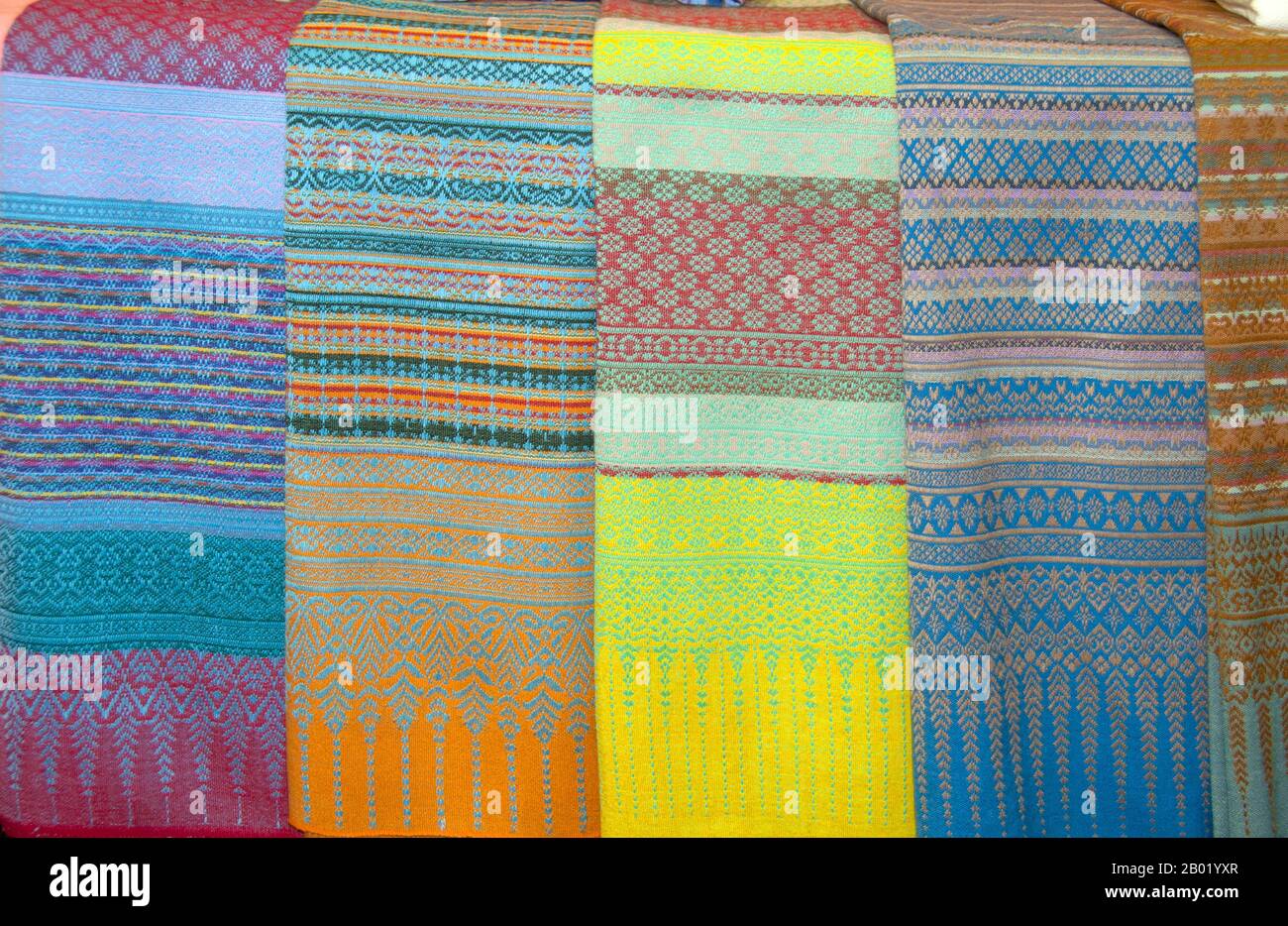 Thailand: PHA Mai Yok Dok Seidenstoffe zum Verkauf auf dem Markt auf Lamphuns traditioneller überdachter Holzbrücke in der Nähe von Wat Phra That Haripunchai, Nordthailand. PHA Mai Yok Dok ist ein aufwendig gewebtes Material nach traditioneller Methode. Ursprünglich am nördlichen Königshof verwendet, wurde sie während der Regierungszeit von König Rama VI. Populär. Die besondere Handwerkskunst und die Fertigkeiten bei der Herstellung dieser Seide haben sie bei denjenigen beliebt gemacht, die traditionelle Designs bevorzugen. Lamphun war die Hauptstadt des kleinen, aber kulturell reichen Mon-Königreichs Haripunchai von etwa 750 n. Chr. bis 1281. Stockfoto
