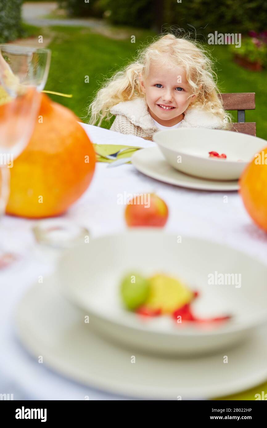 Lächelndes blondes Mädchen sitzt an einem festgelegten Tisch im Garten Stockfoto