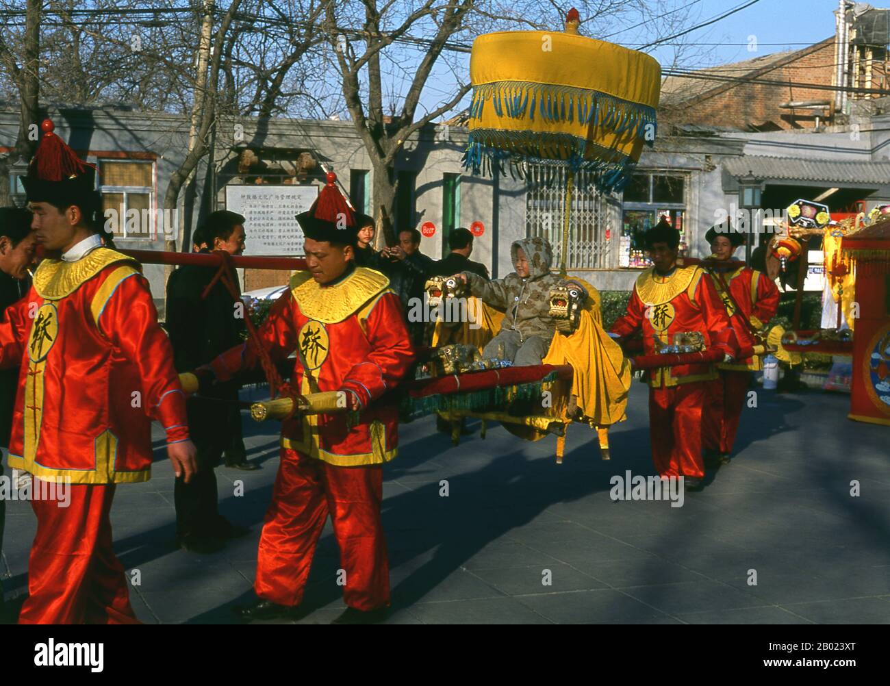 China: Ein Kind wird auf einem kunstvoll geschmückten Palanquin vor dem Glockenturm (Zhonglou) in Peking präsentiert. Der Trommelturm (Gǔlóu) und der Glockenturm (Zhōnglóu) wurden 1272 während der Regierungszeit von Kublai Khan (R. 1260–1294) errichtet. Kaiser Yongle (R. 1402–1424) baute die Türme 1420 wieder auf und sie wurden während der Regierungszeit des Qing-Kaisers Jiaqing (R. 1796–1820) wieder renoviert. Sowohl der Drum- als auch der Glockenturm wurden während der Yuan-, Ming- und Qing-Dynastien als Zeitmesser genutzt. Stockfoto