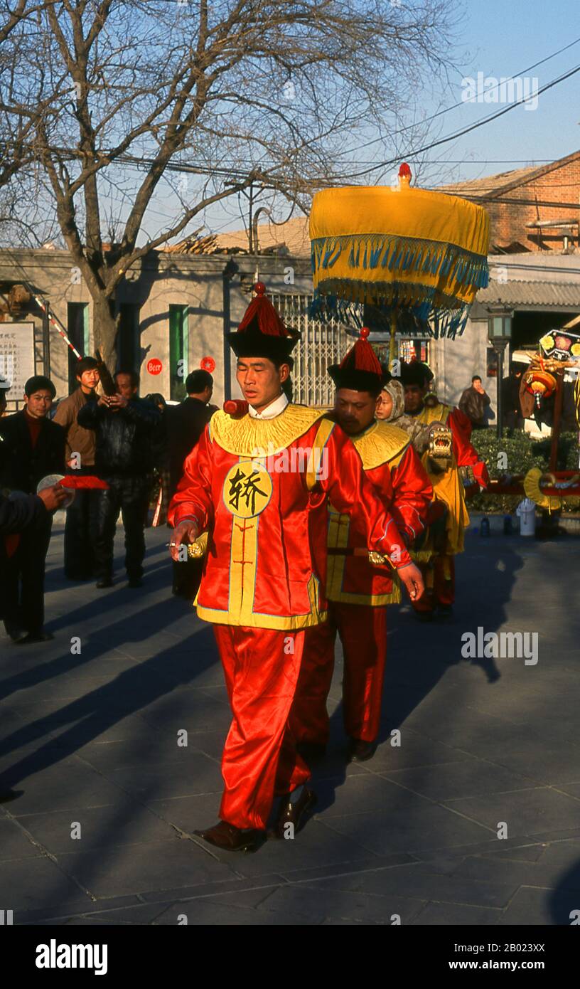 China: Ein Kind wird auf einem kunstvoll geschmückten Palanquin vor dem Glockenturm (Zhonglou) in Peking präsentiert. Der Trommelturm (Gǔlóu) und der Glockenturm (Zhōnglóu) wurden 1272 während der Regierungszeit von Kublai Khan (R. 1260–1294) errichtet. Kaiser Yongle (R. 1402–1424) baute die Türme 1420 wieder auf und sie wurden während der Regierungszeit des Qing-Kaisers Jiaqing (R. 1796–1820) wieder renoviert. Sowohl der Drum- als auch der Glockenturm wurden während der Yuan-, Ming- und Qing-Dynastien als Zeitmesser genutzt. Stockfoto