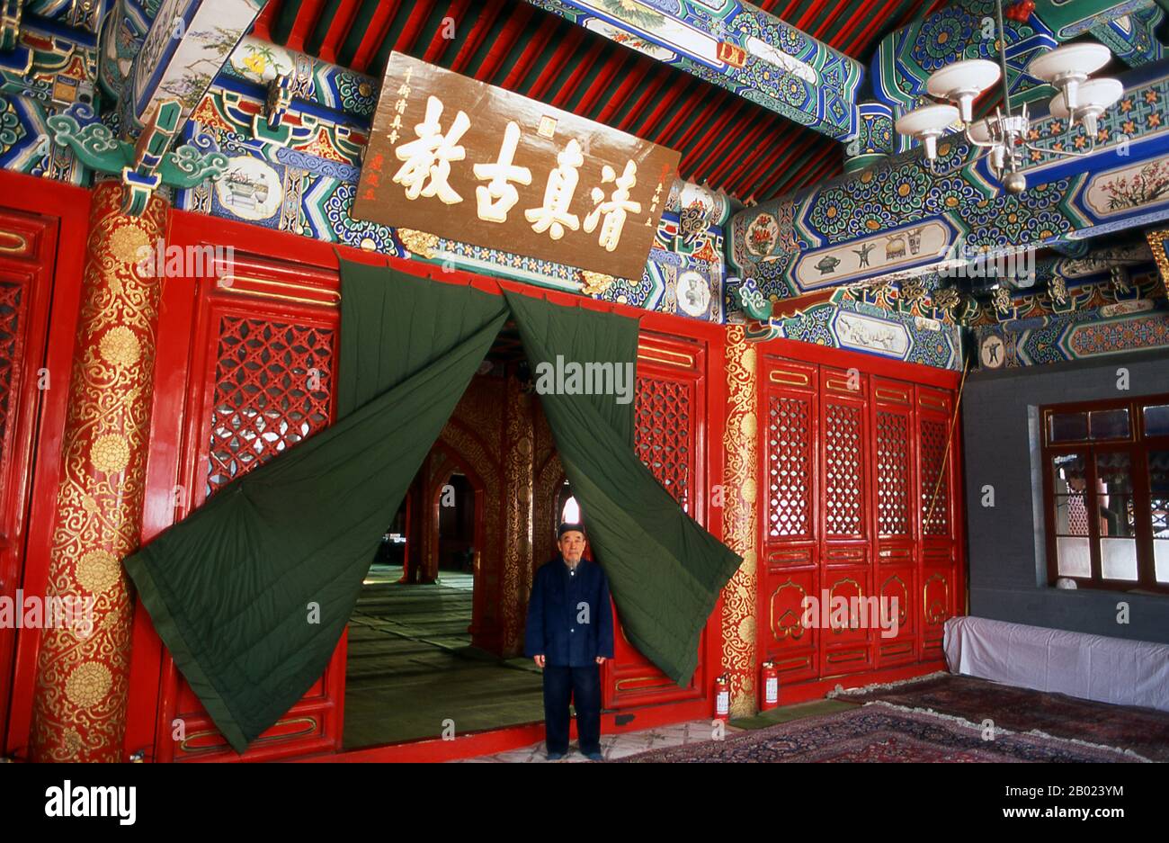 China: Der Imam am Eingang des Gebetssaals, Ox Street Mosque oder Cow Street Mosque (Niujie Mosque), Peking. Die Ox Street Mosque oder Cow Street Mosque wurde 966 erbaut. Sie wurde 1215 von Dschingis Khan zerstört. Der Wiederaufbau der Moschee erfolgte während der Regierungszeit des Qing-Kaisers Kangxi (R. 1661–1722). Die Moschee hat alle üblichen Merkmale von Moscheen, die anderswo auf der Welt zu finden sind - Minarett, Gebetshalle gegenüber Mekka, arabische Inschriften - die Gebäude selbst sind eindeutig chinesisch. Sie ist die größte und älteste Moschee Pekings. Stockfoto