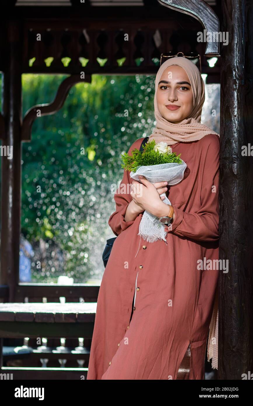 Junge Frau im Hijab, die Blumen in islamischer Kleidung hält Stockfoto