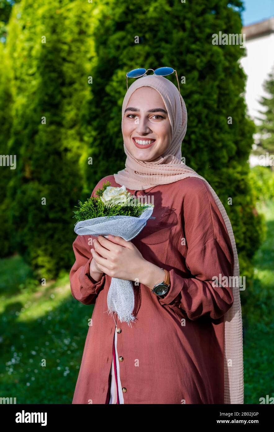 Junge Frau im Hijab, die Blumen in islamischer Kleidung hält Stockfoto