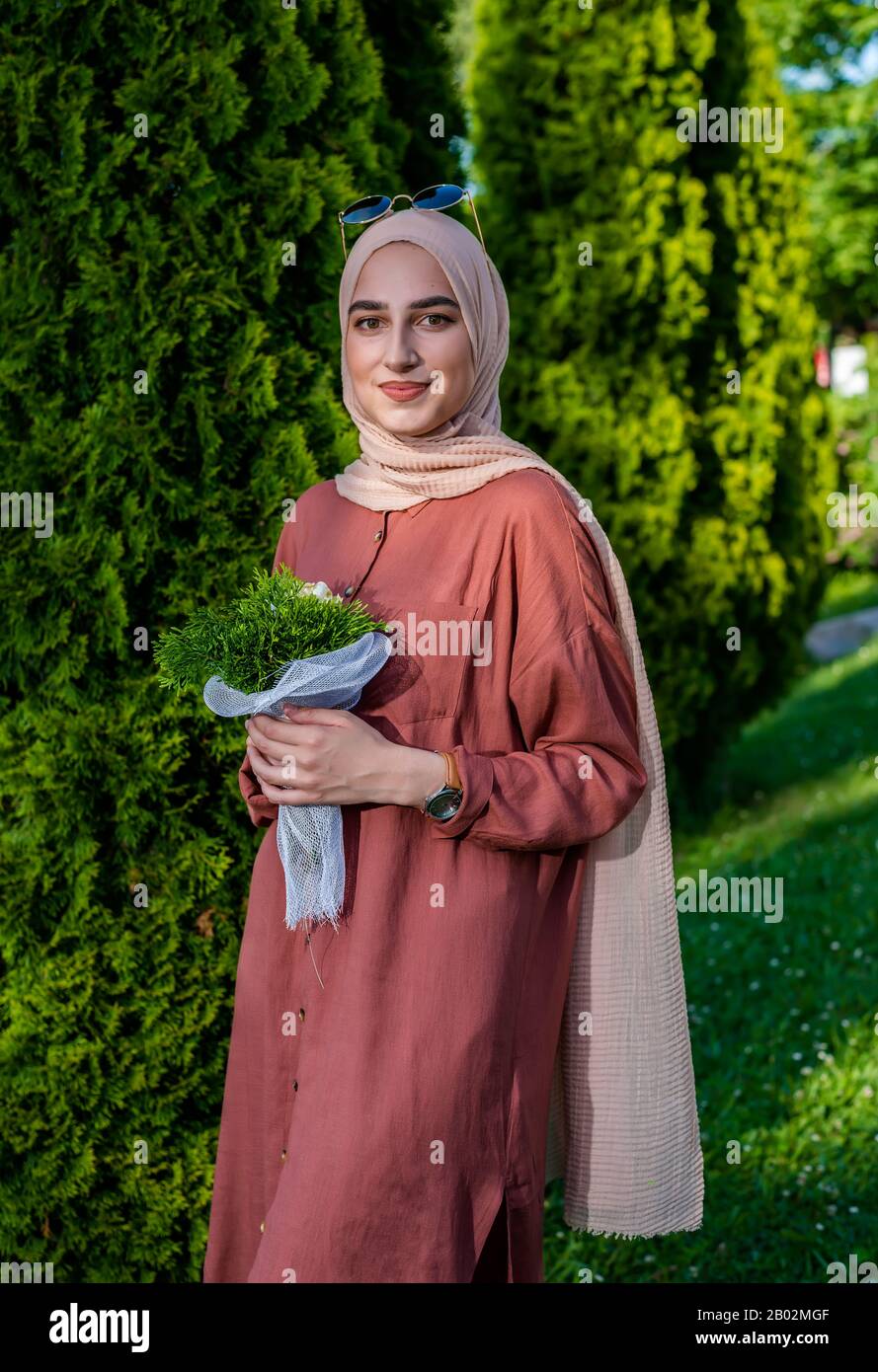Junge Frau im Hijab, die Blumen in islamischer Kleidung hält Stockfoto
