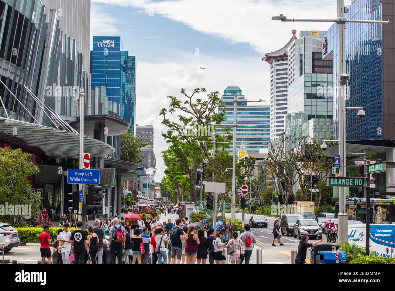 Straßenszenen der Orchard Road gefüllt mit Hotels, Menschenmenge, einem Einkaufsgürtel und einem Flugzeug passiert, um am Himmel vorbeifliegen. Singapur. Stockfoto