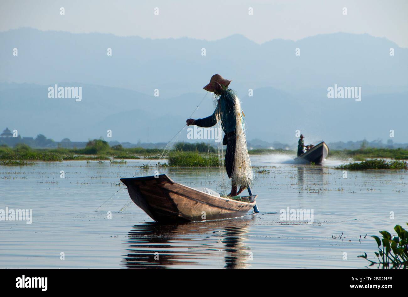 Der Inle Lake (116 km2) ist flach, lang, kristallklar und ruhig. Hier leben die Intha-Menschen, die auf beiden Seiten von hohen Hügeln eingehüftet sind. Die Intha-Männer sind dafür berühmt, dass sie mit einem Bein aufstehen, während sie mit hohen, konischen fallen für Inle-Karpfen und den anderen, kleineren Fischen, mit denen der See schwärmt, angeln. Die Intha-Frauen, die Marktgärtner sind, nutzen den fruchtbaren Boden rund um den See sowie schwimmende Inseln aus Wasserhyazinthen und Schlamm, um Blumenkohl, Tomaten, Gurken, Kabbagen, Bohnen und Auberginen anzubauen. Inle ist ein einfacher Ort, aber ein Ort mit viel - beides erholsam Stockfoto