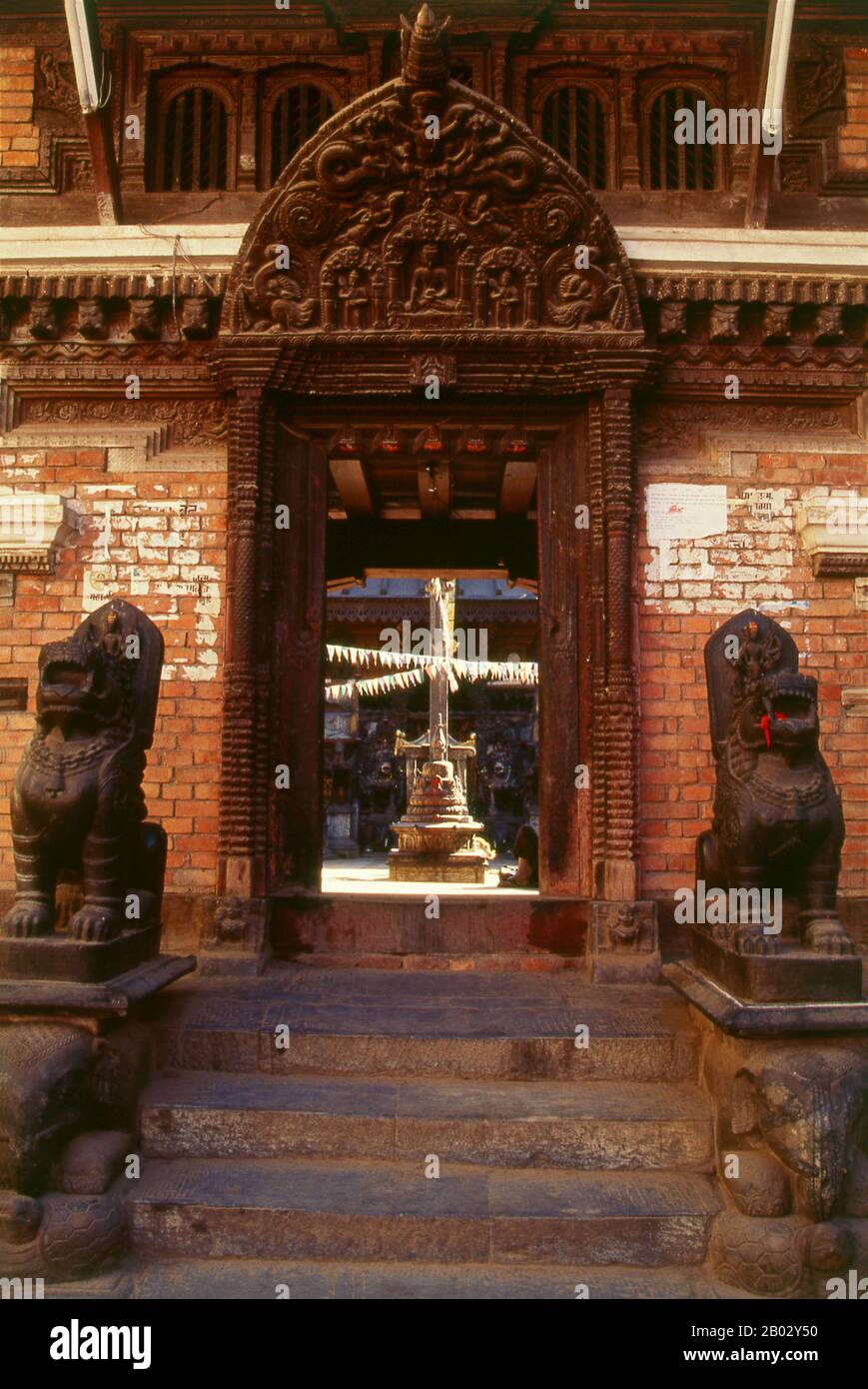 Rudravarna Mahavihara, oder Oku Bahal, wurde Mitte des 17. Jahrhunderts erbaut. Der Tempel befindet sich um einen Innenhof, der mit Chaitya- und Metallfiguren aller Art und Größen überströmt ist. Es gibt massive Garudas, Elefanten, Pfauen, Figuren betender Anbeter und eine Statue von Juddha Shamsher Rana, die dem Tempel nach dem Erdbeben von 1934 großzügige Wiederherstellungshilfen gewährt haben. In den Ecken des mit Öllampengeländern gesäumten Innenhofes befinden sich Bronzefiguren des boshaften affengottes Hanuman, die ihm beim Verzehr eines Kürbisses, einer Banane und etwas zeigen, das wie ein aussieht Stockfoto