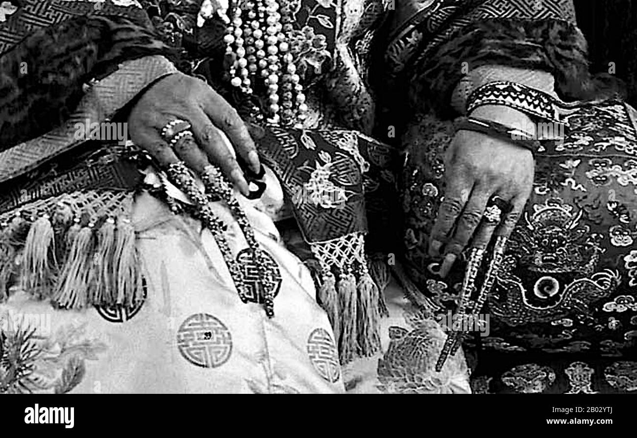 Westliche Beschreibungen chinesischer Kaiser, Königtum und Adeliger erwähnen oft lange Fingernägel, die die Person über jede Möglichkeit manueller Arbeit markieren. Diese Fingernagel-Protektoren oder Schutzvorrichtungen können als einzelnes Juwel an der Hand oder in mehreren Sätzen getragen werden. Laut dem San Diego Museum of Art: "Fingernagelschützer wurden von einer sehr elitären Gruppe getragen - Mandschu-Hofdamen der späten Qing-Dynastie. Obwohl Gelehrte chinesischer Trachten in der Regel Fingernagelschützer in die Qing-Dynastie datieren, sind sie tatsächlich erst für das späte 19. Porträts der frühen Qing Court Ladies Stockfoto