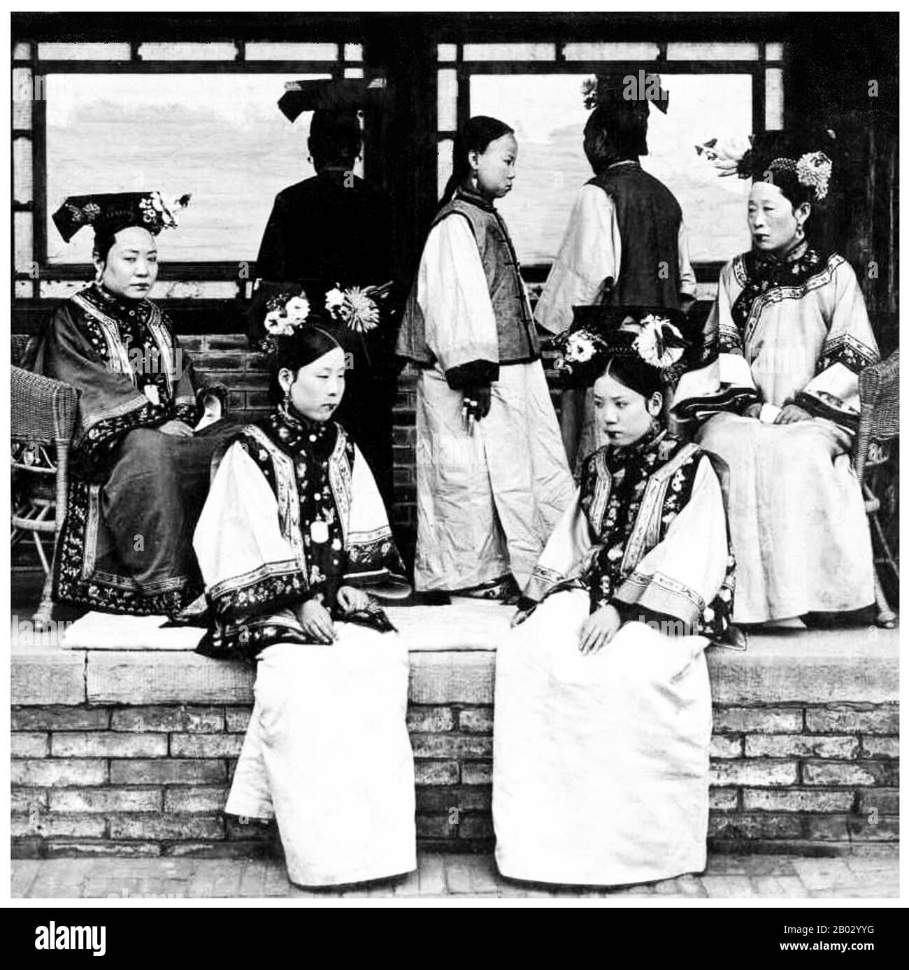 Manchu Frauen der Verbotenen Stadt oder Gugong in Peking posieren für ein Foto c. 1910 in den letzten Tagen der Mandschu Qing-Dynastie (1644-1911). Sie tragen aufwendige und teure Kleider. Ihre Gesichter sind mit Pulver weiß, und ihr Lippenstift wird nach der Mode der Zeit in einem schmalen Band über die Mitte ihrer Lippen aufgetragen. Stockfoto