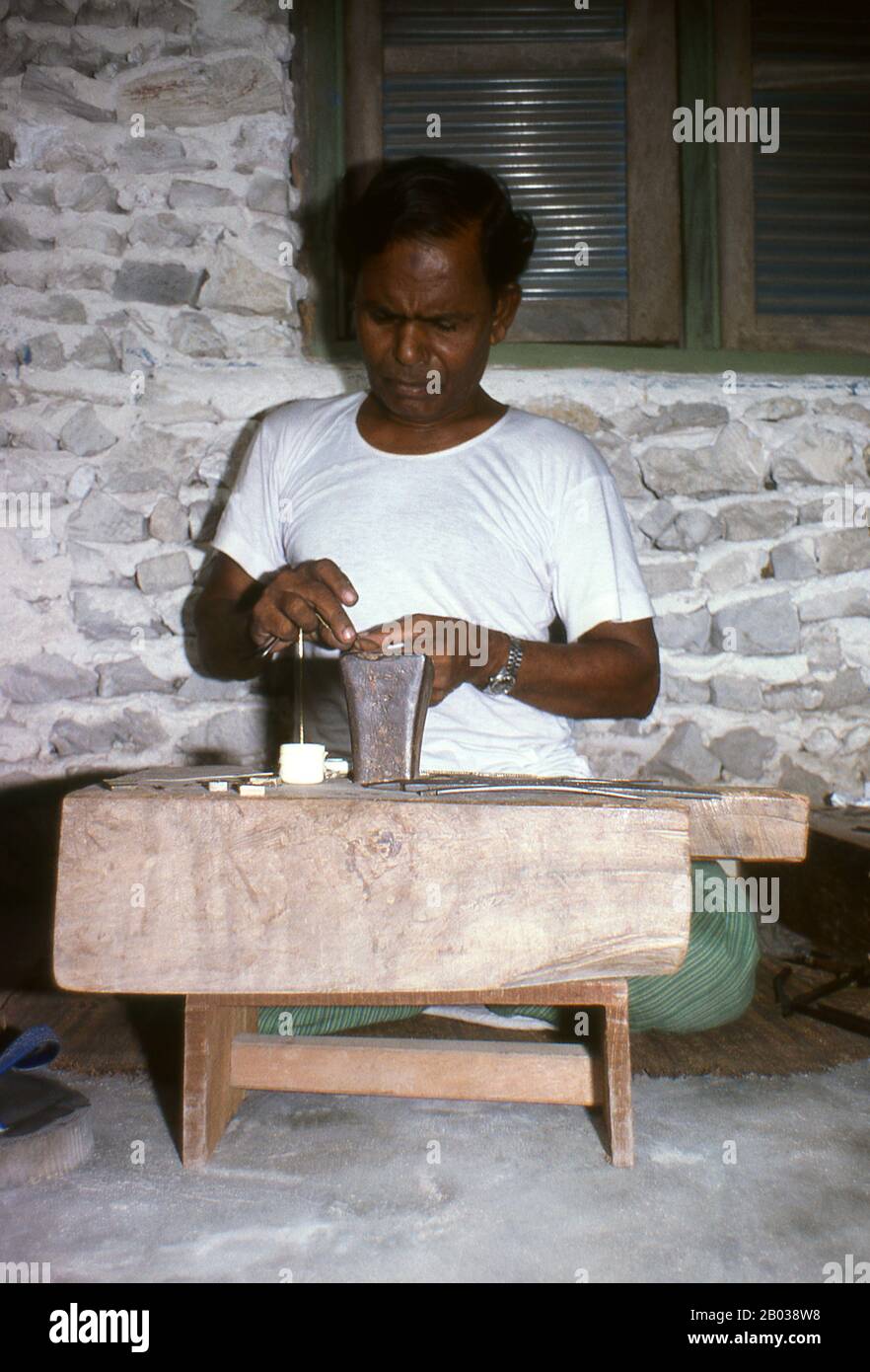 Am östlichen Rand des Süd-Nilandhoo-Atolls liegt die winzige Insel Rinbudhoo. Hier, in einem der ruhigsten und saubersten Dörfer der Malediven, lebt die einzige Gruppe der erblichen Goldschmiede des Landes. Sie schmelzen viktorianische Goldschürfer und Marie-Therèse-Taler so beiläufig wie kürzlich importierte Minispannen aus Dubai, sie stellen eine exquisite Auswahl an Ketten, Halsketten, Ohrringen, Fingerringen und Amuletten her. Asiens kleinste und am wenigsten bekannte Nation, die Republik Malediven, liegt verstreut von Nord nach Süd über einen 750 Kilometer langen Lauf des Indischen Ozeans 500 Kilometer südlich von wes Stockfoto