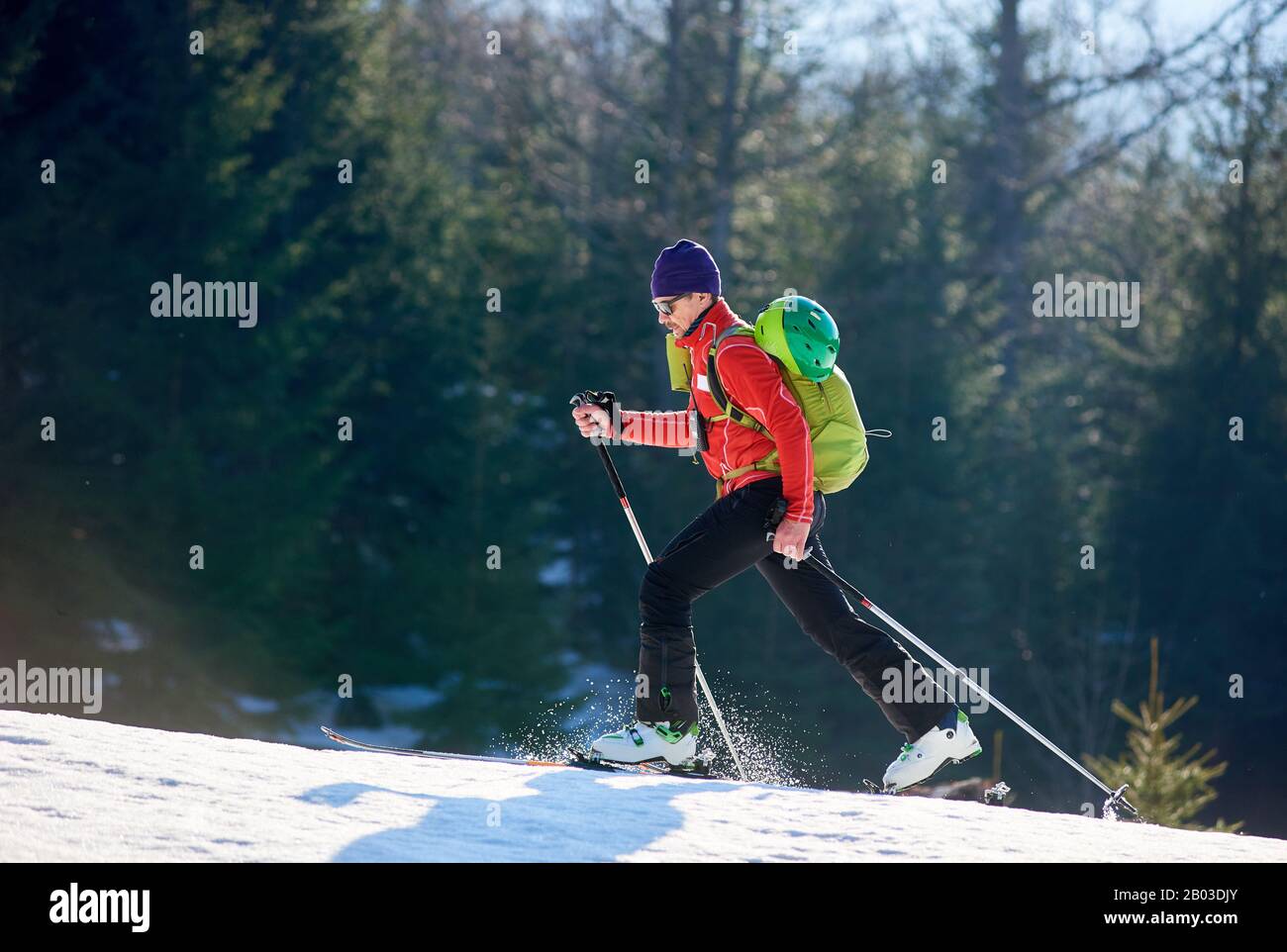 Mann allein mit Ski auf dem Berg. Kerl mit Rucksack auf einem verschwommenen Waldhintergrund am sonnigen Tag. Ski-Saison und Wintersportkonzept Stockfoto