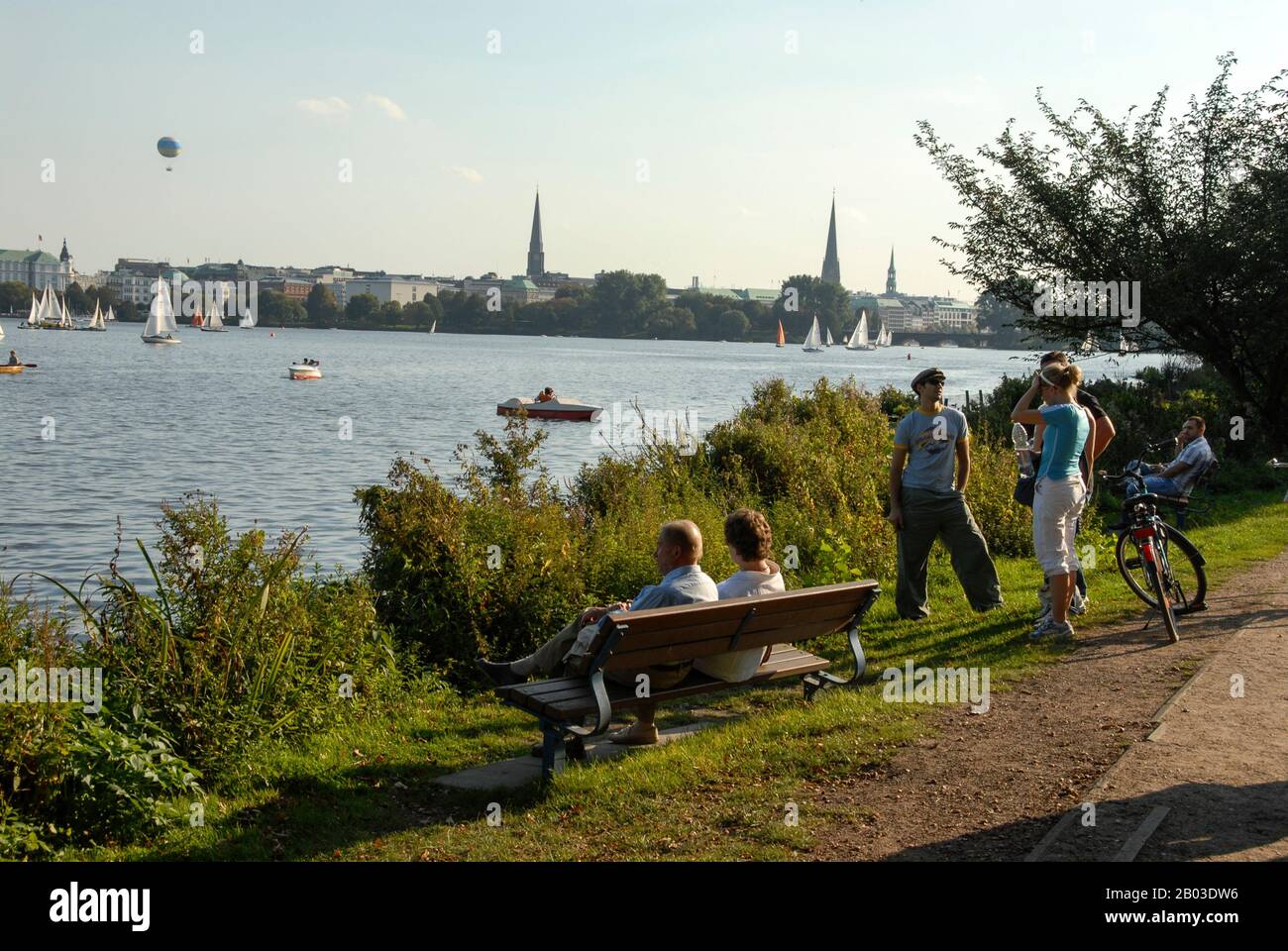 Besucher und Einheimische genießen die Sonne am Alsterinnensee im Zentrum Hamburgs, Norddeutschland. In der Ferne befindet sich ein Heißluftballon Stockfoto