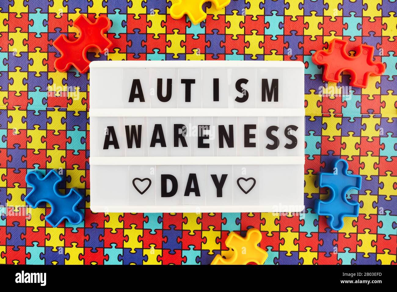 Leuchtkasten mit Welt Autismus Bewusstsein Tag Text auf farbigen Puzzle-Hintergrund. Draufsicht Stockfoto