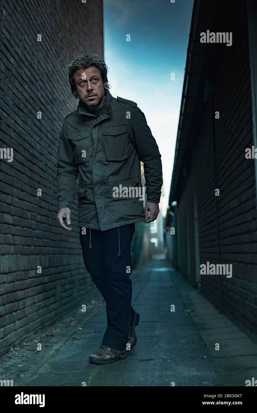 Verdächtiger Mann, der in einer dunklen städtischen Gasse spazieren ging. Stockfoto