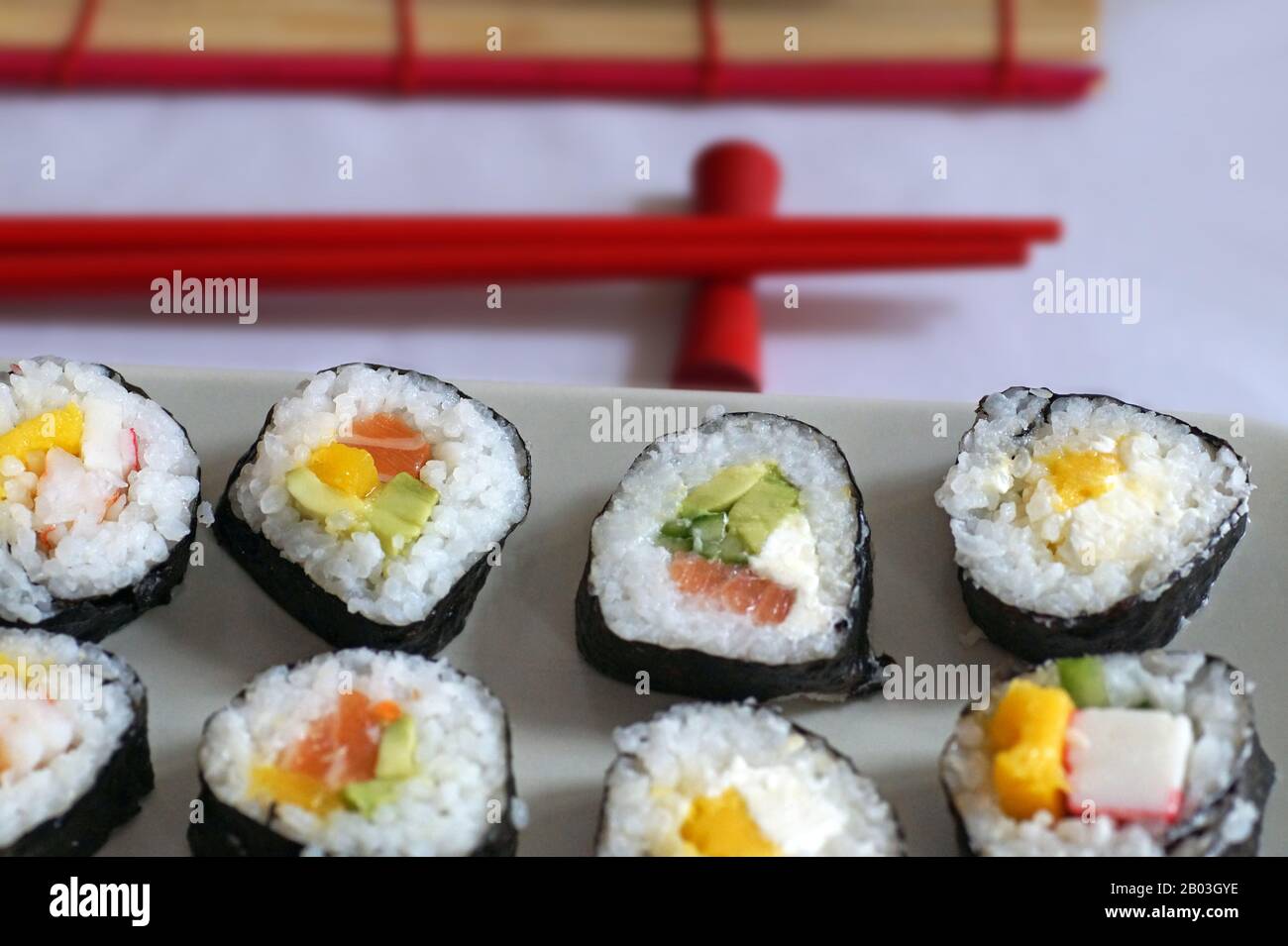 Matte und Essstäbchen. Verschiedene Sushi-Typen werden auf einer rechteckigen Platte serviert. Stockfoto