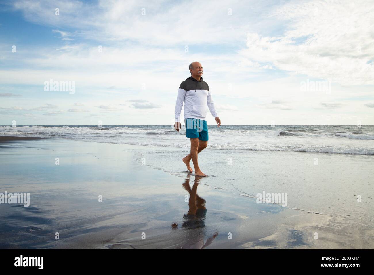 Ein älterer Mann, der am Strand spazieren geht Stockfoto