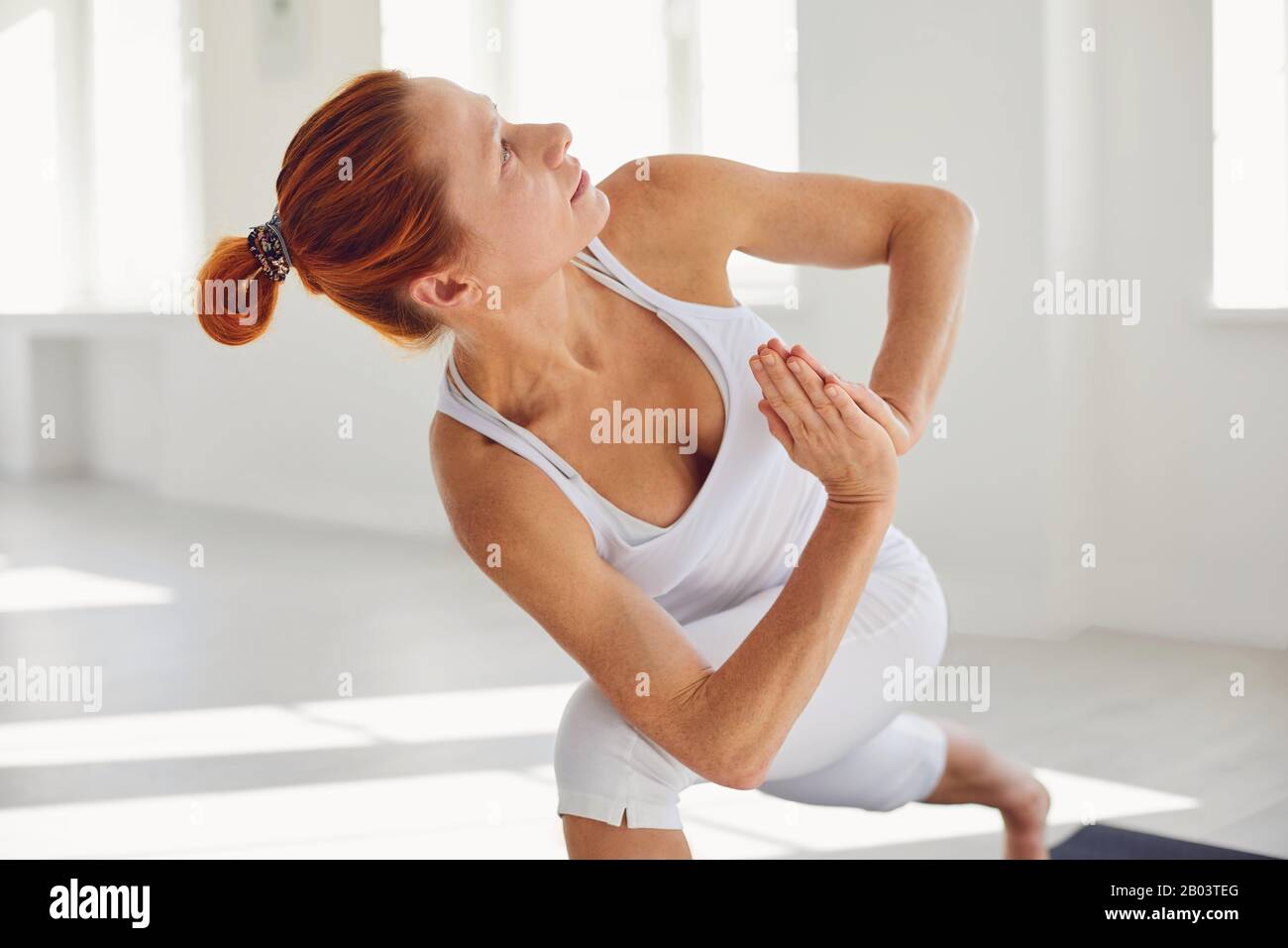 Yoga-Mädchen. Eine Frau in weißer Sportswear übt Yoga-Balance in einem grauen Raum aus. Stockfoto