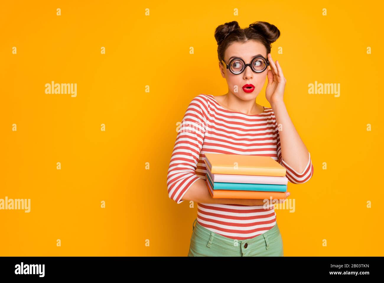 Foto der Studentendame halten viele Bücher aussehen Seite leer Raum verängstigt tragen freak Nerd Specs gestreiftes rot weißes Hemd grüne Hosen isoliert leuchtend gelb Stockfoto