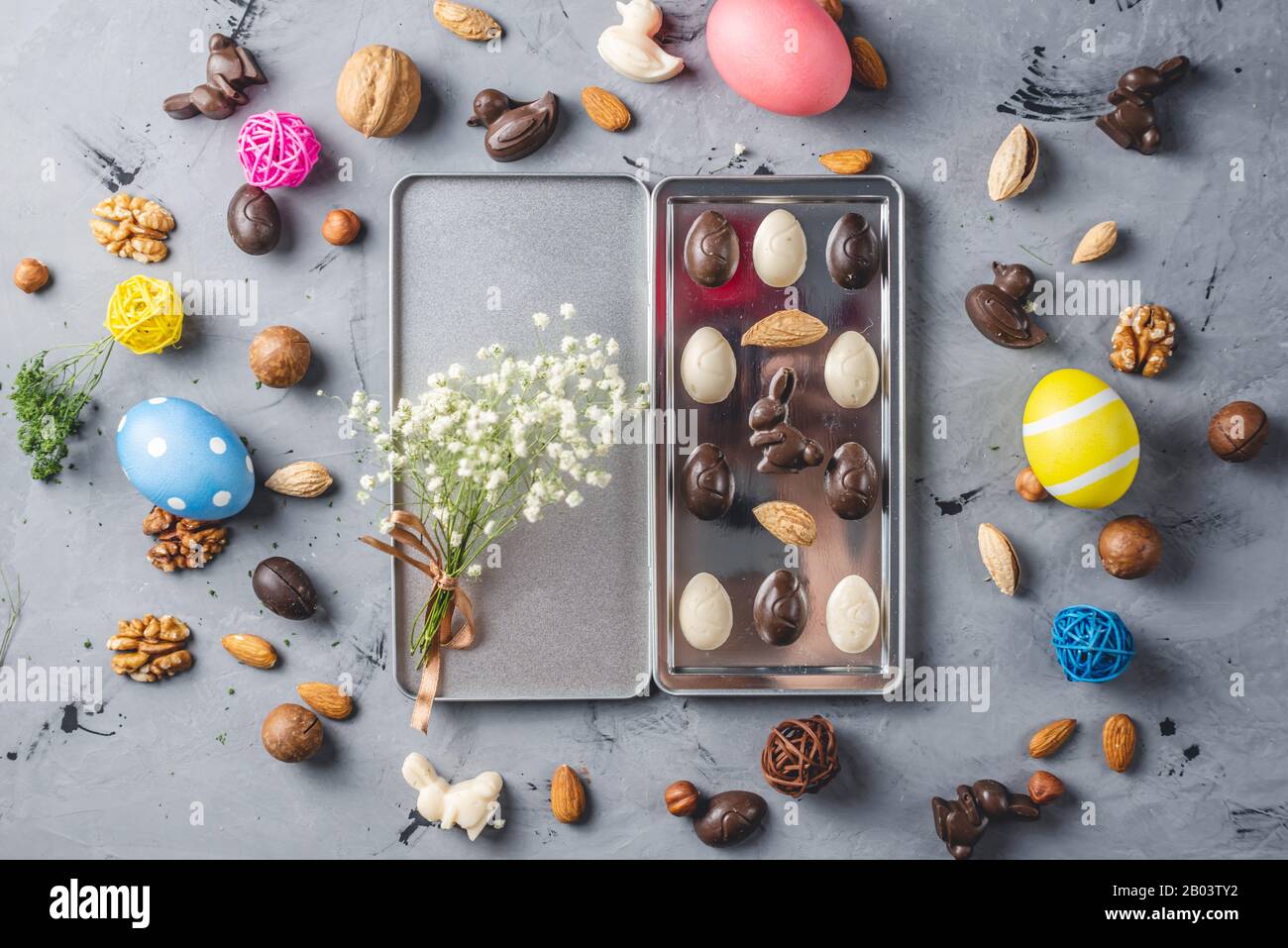 Geschenkset von Schokolade in Form von Eiern und einem Häschen in einer Schachtel mit einem Blumenstrauß aus Frühlingsblumen und hellen Ostereiern Stockfoto