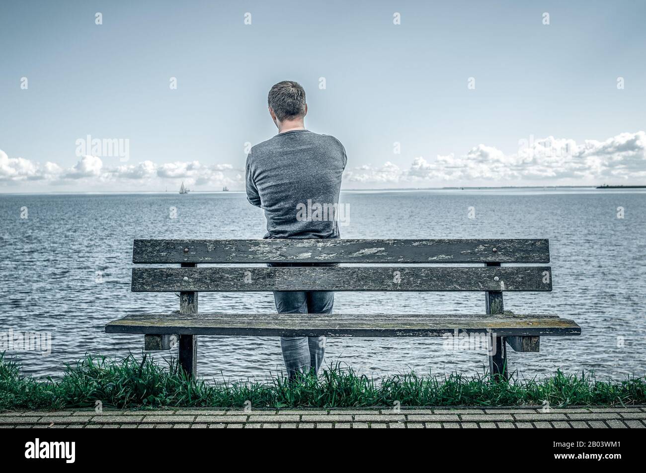 Ein Mann steht an einer Bank am Meer. Stockfoto