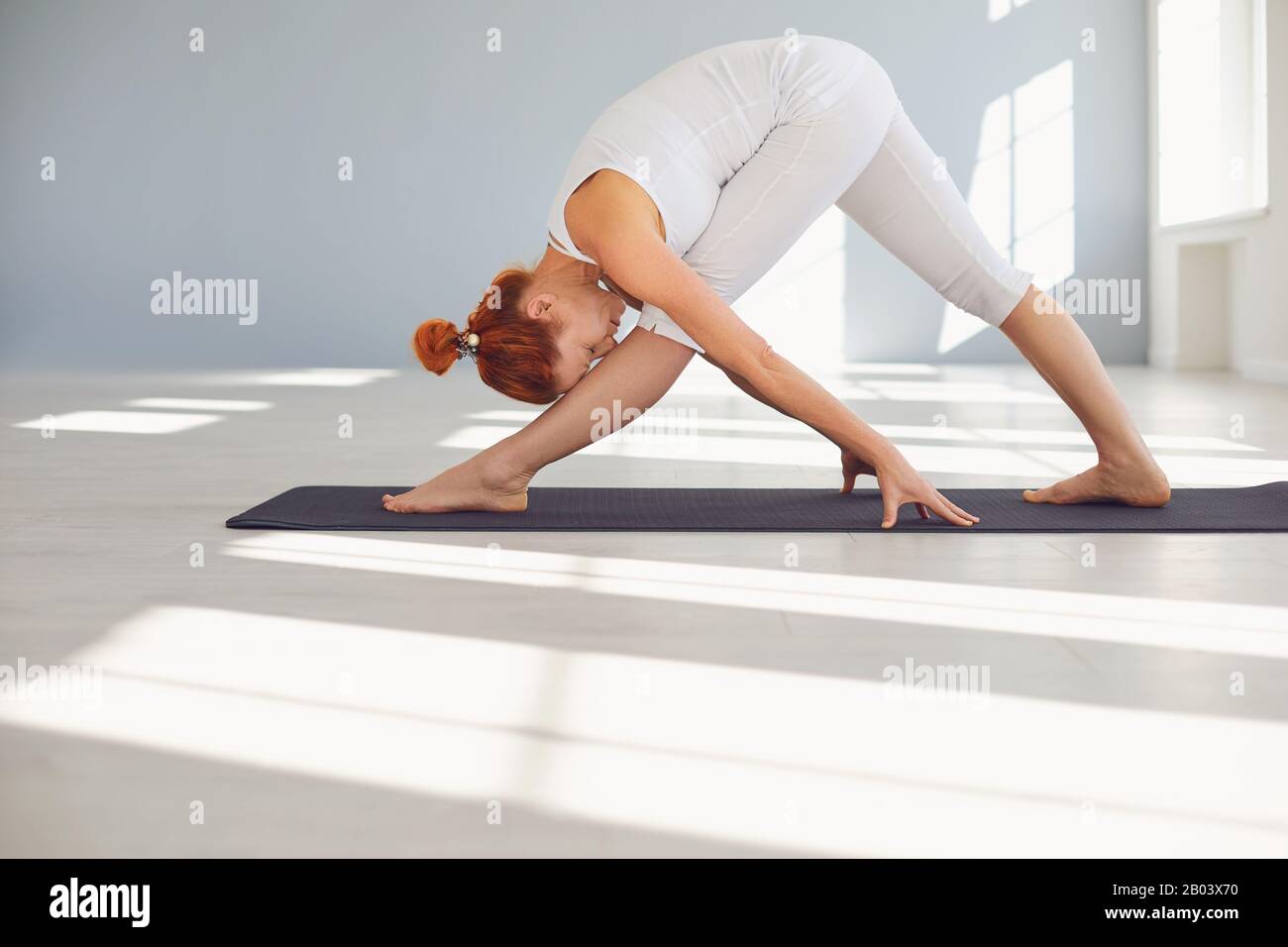Yoga-Mädchen. Eine Frau in weißer Sportswear übt Yoga-Balance in einem grauen Raum aus. Stockfoto