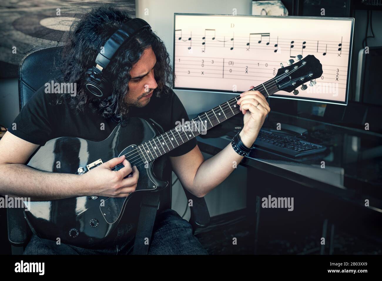 Langhaariger Rockkomponist Musiker man with Headphones spielen E-Gitarre mit musikalischer Partitur auf Bildschirmhintergrund Stockfoto
