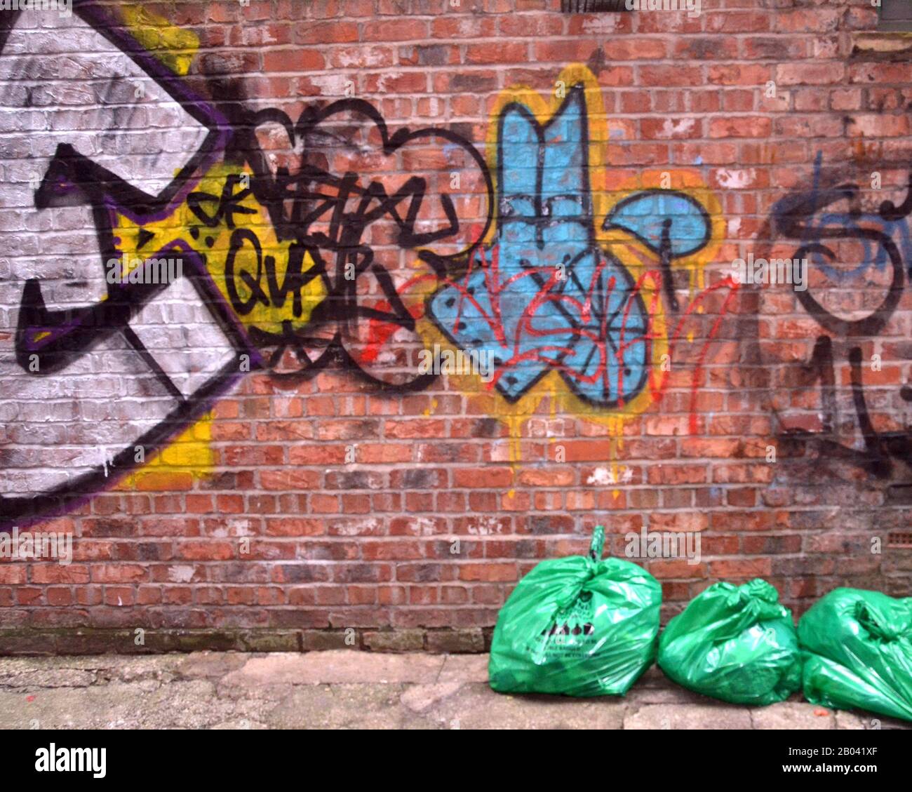 Grüne Müllsäcke vor Kunstwerken und Graffiti schmücken Straßen im Stadtteil Northern Quarter in Manchester, Großbritannien Stockfoto