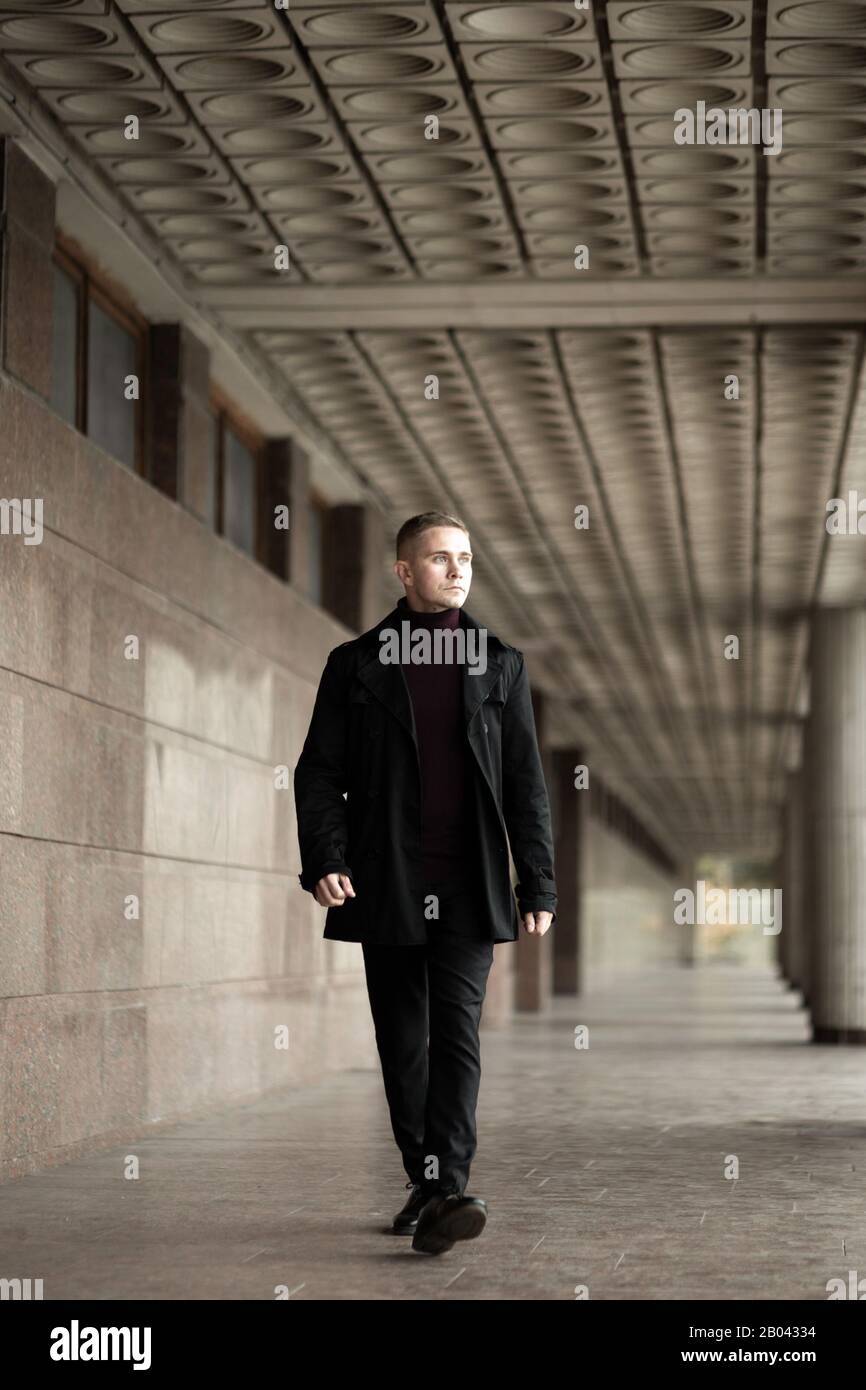 Stilvoller Mann mit schwarzem Trenchcoat und Polokragen am modernen Gebäude Stockfoto