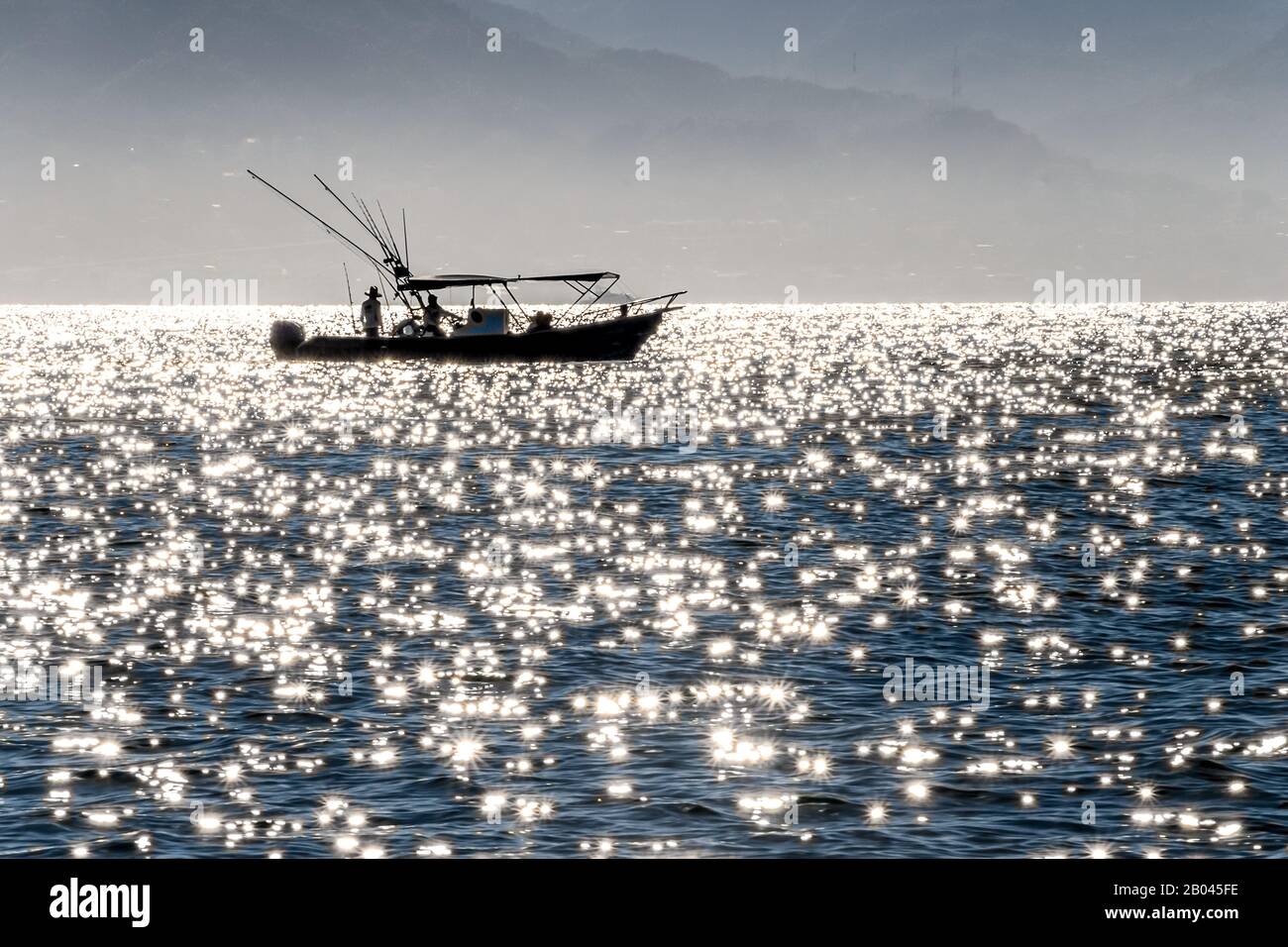 Entfernte Silhouette eines Fischerboots inmitten von Glitzern im Meer, Puerto Vallarta, Jalisco, Mexiko, am frühen Morgen Stockfoto
