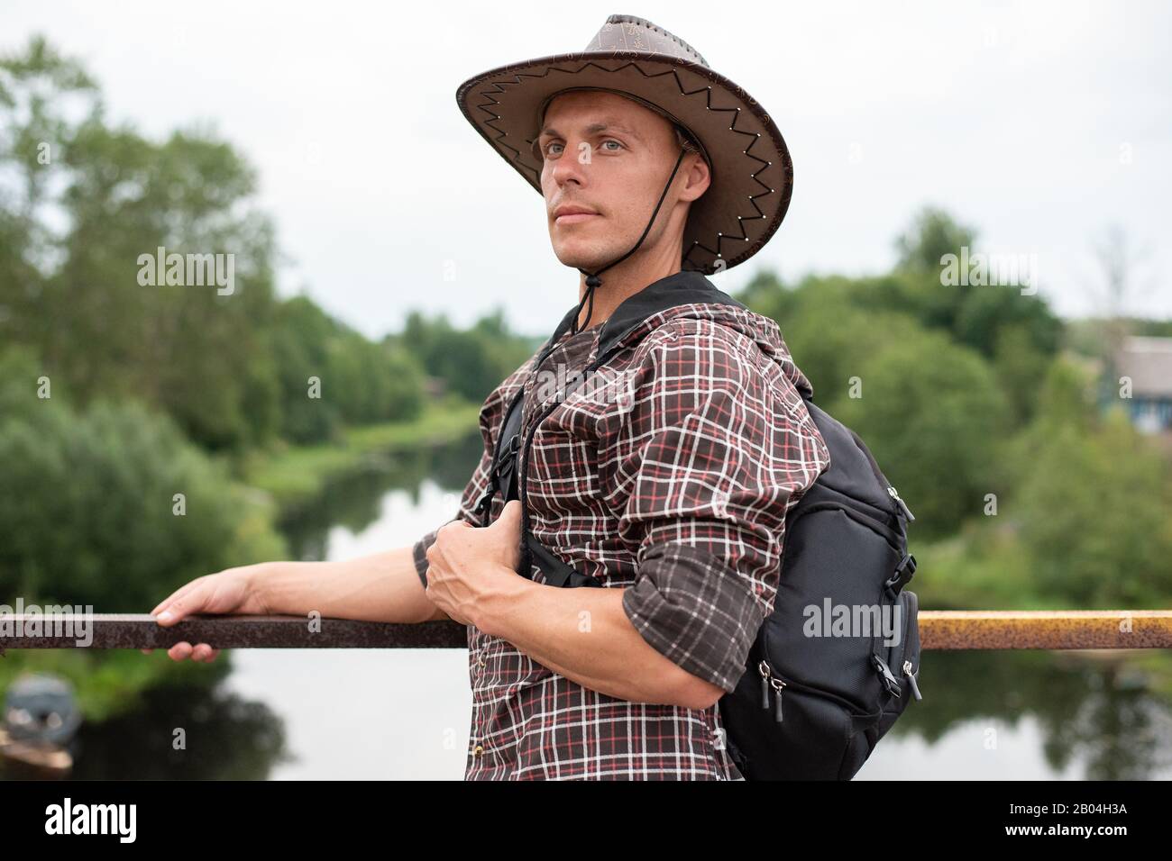 Ein Mann in einem Cowboyhut, mit einem Rucksack auf der Brücke über den Fluss. Stockfoto