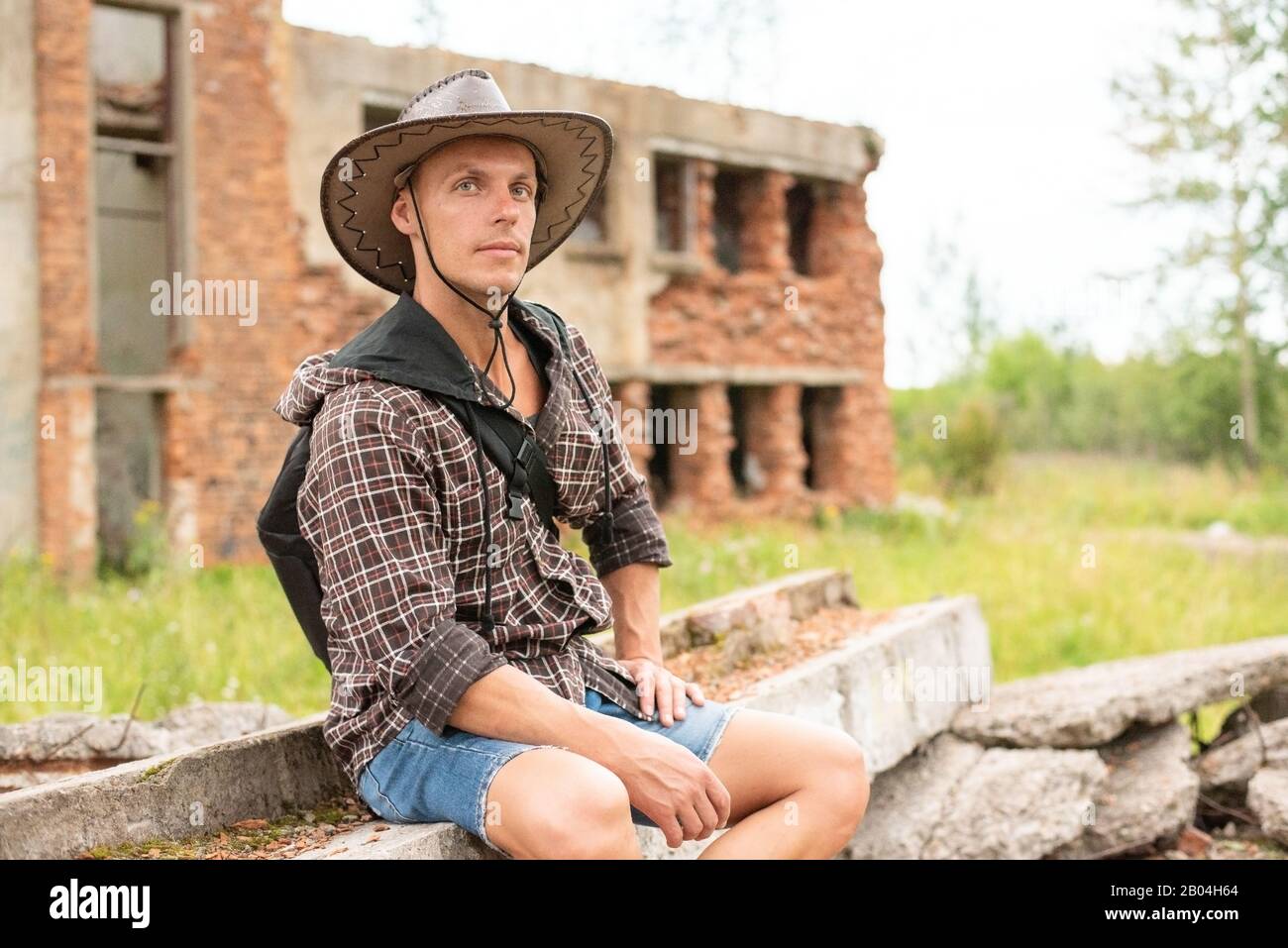 Ein Mann in einem Cowboyhut sitzt inmitten eines zerstörten Hauses. Stockfoto