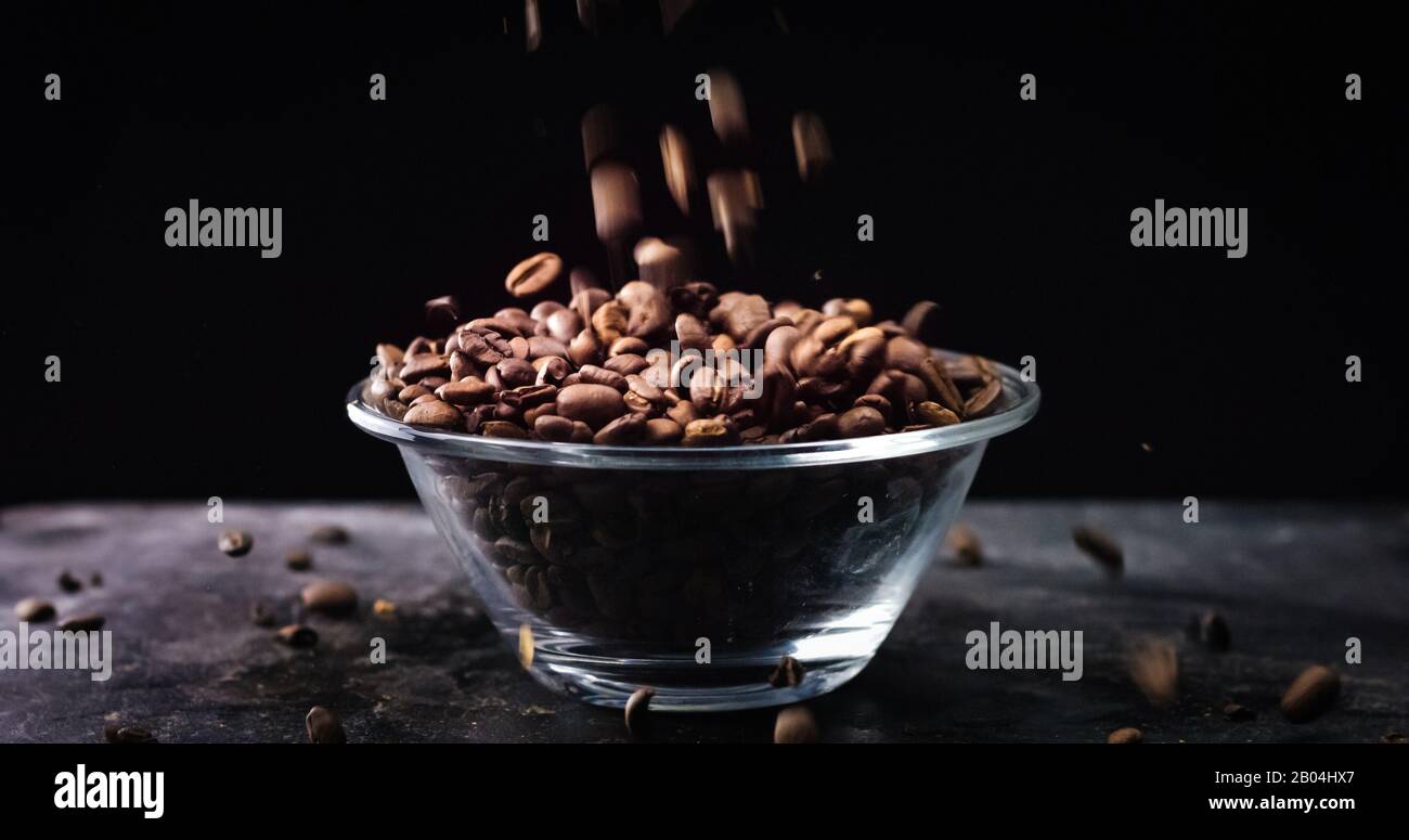 Gebratene Kaffeebohnen, die in einer Glasschale auf schwarzem Grund fallen. Stockfoto