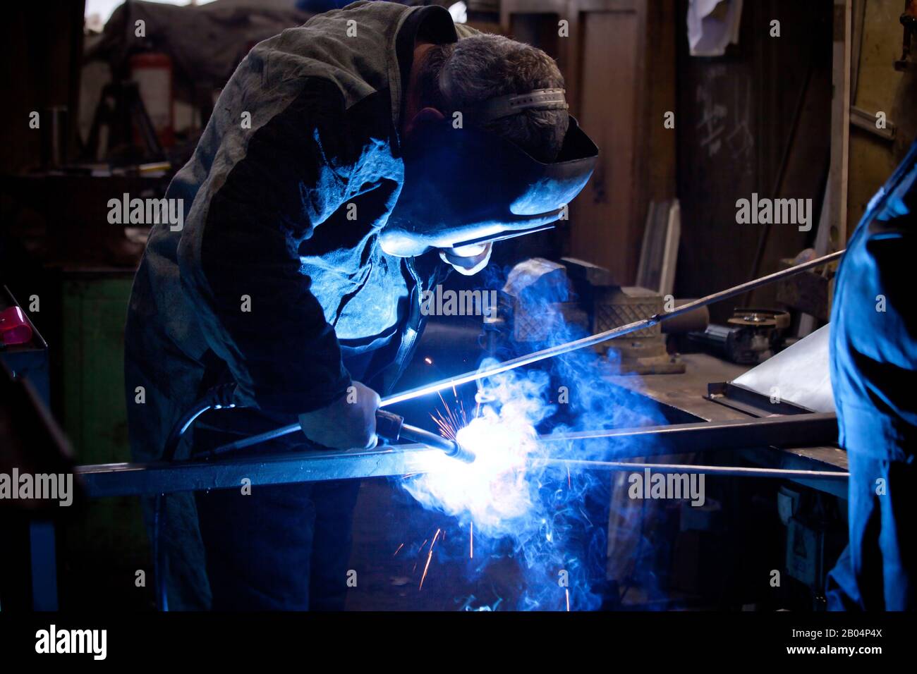 Unanstiraler Arbeiter in Maske, beim Schweißen von Metall mit hellem Licht, Rauch und Funken Stockfoto