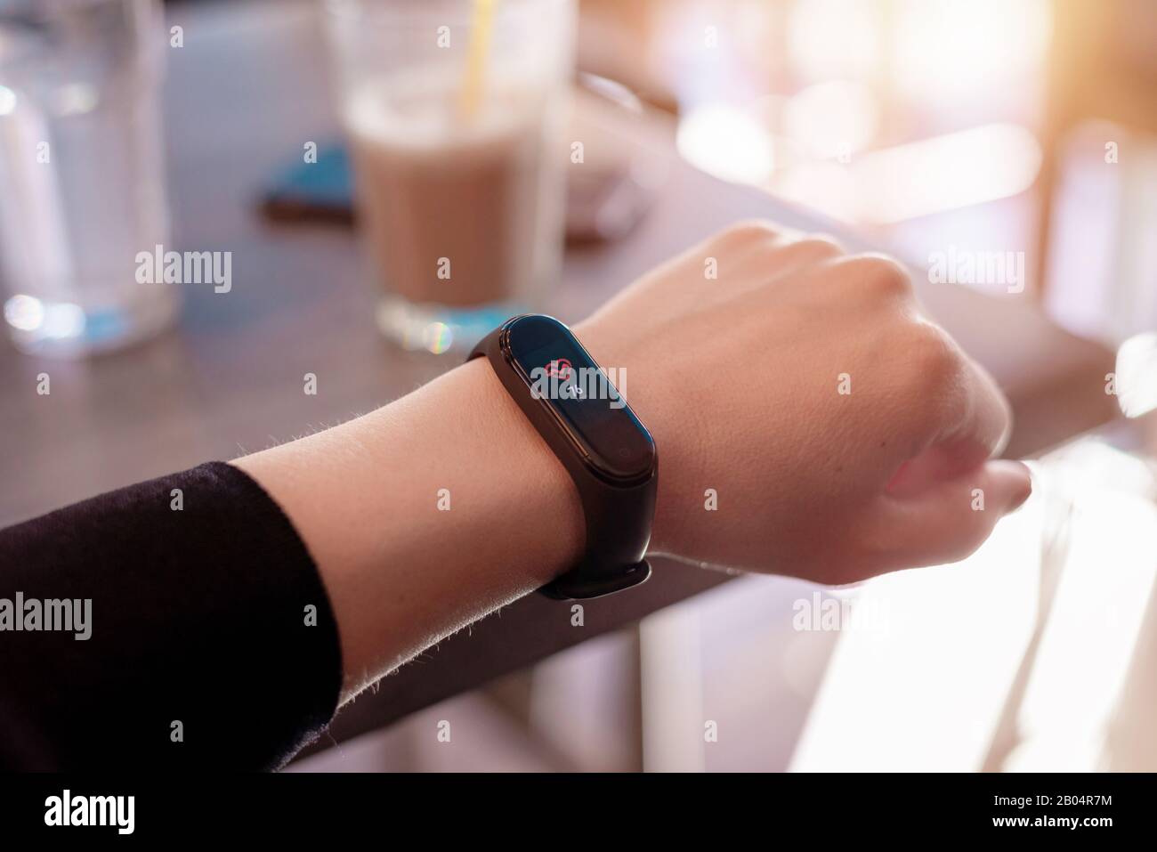 Mädchen misst ihre Herzfrequenz mit einem intelligenten Armband. Nahaufnahme. Café-Bar im Hintergrund Stockfoto