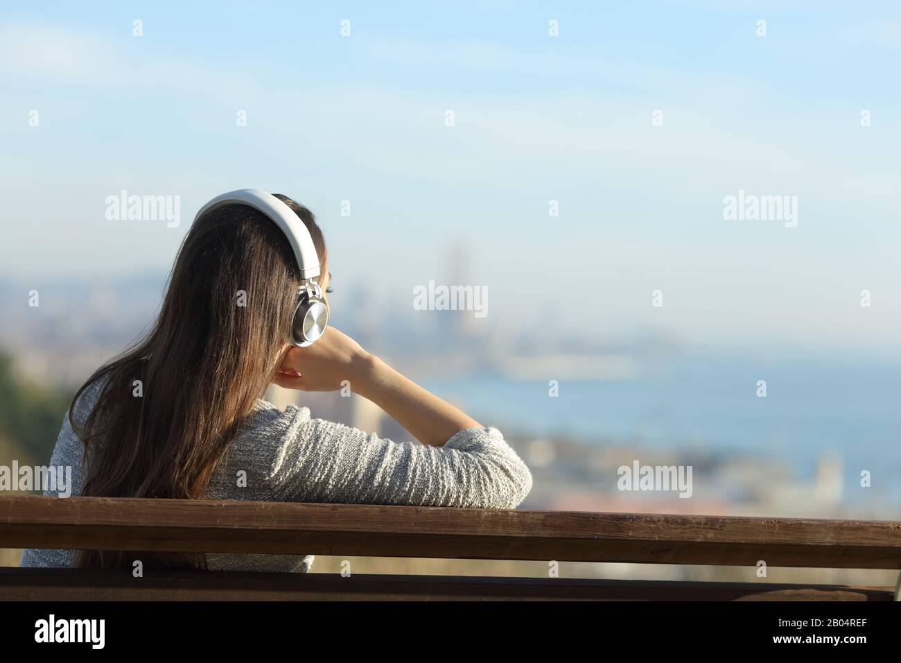 Rückansicht einer entspannten Frau, die Musik hört und Kopfhörer trägt, die die Blicke auf die Randgebiete der Stadt beschaulich sind Stockfoto