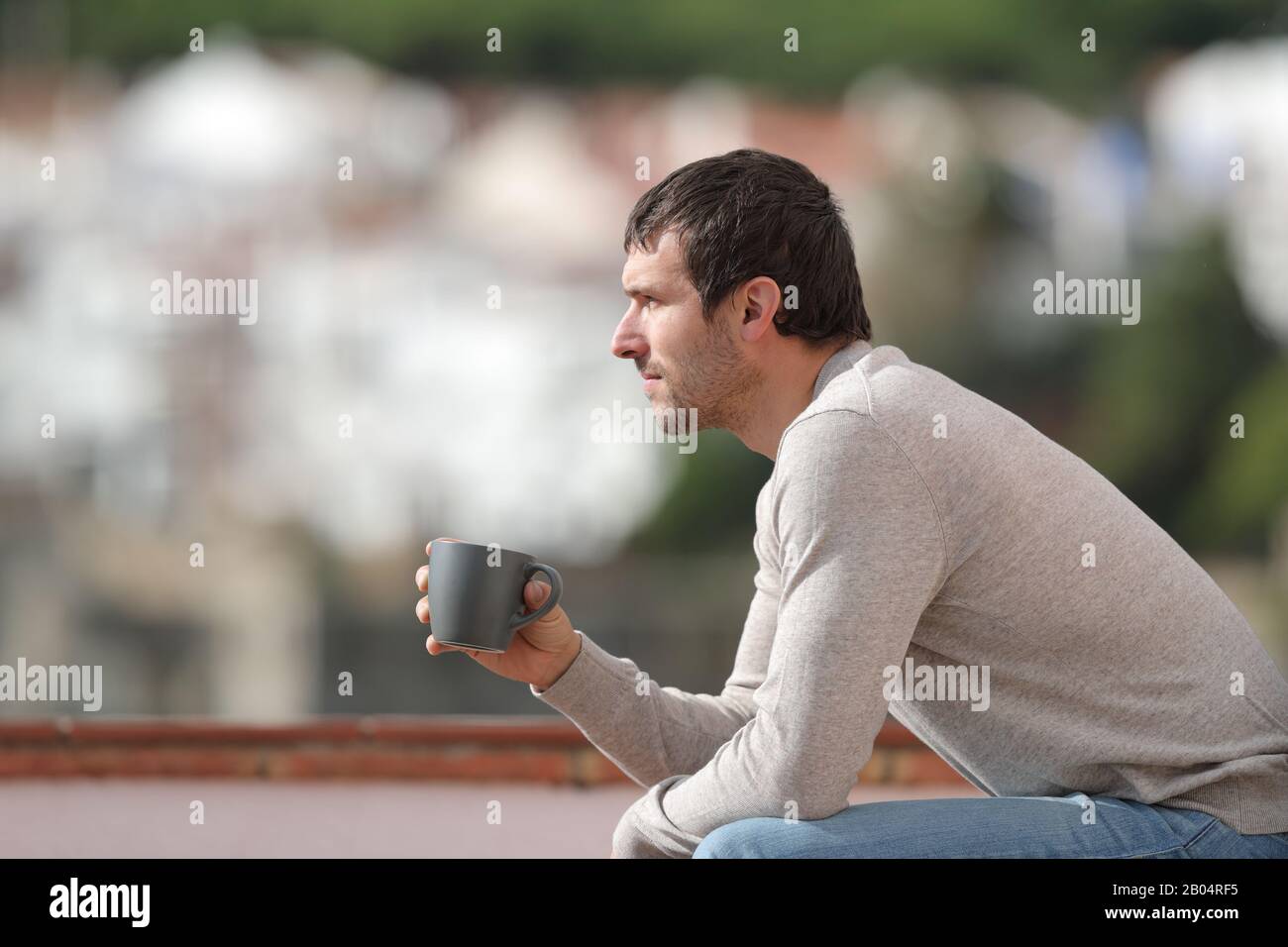 Seitenansicht Porträt eines ernsthaften Mannes, der auf einer Bank sitzt, die die Kaffeetasse hält und die Blicke in einer Stadt betrachtet Stockfoto